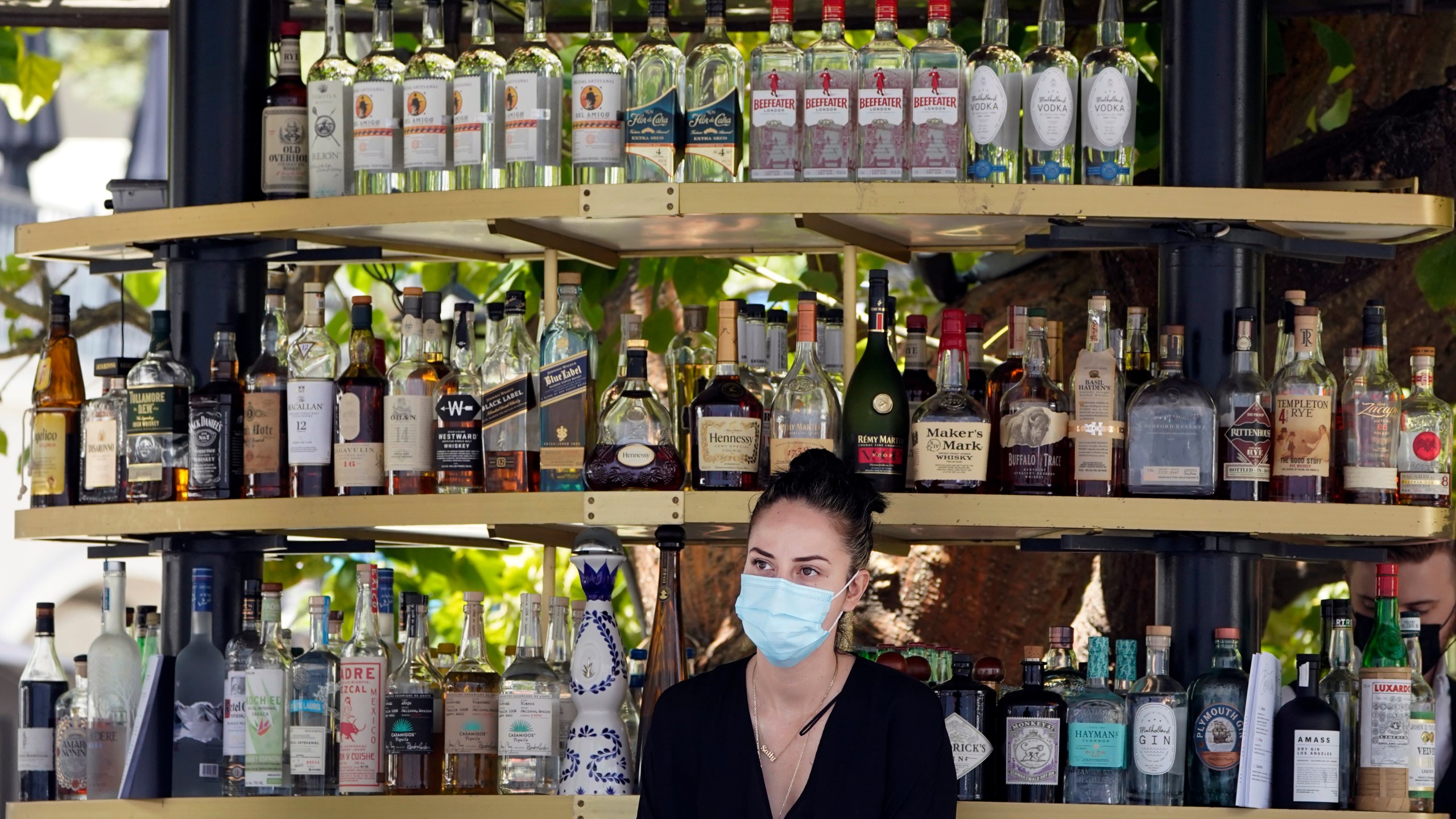 A bartender wears a mask while working at an outdoor bar amid the COVID-19 pandemic Thursday, May 20, 2021, at The Grove in Los Angeles. California regulators will shoot for a mid-June easing of workplace masking and social distancing requirements to conform with a broader state order. They asked to delay a debate Thursday on how quickly they should drop coronavirus safety rules for employees. (AP Photo/Marcio Jose Sanchez)