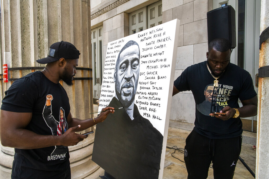 Artist Dennis Owes, 31, from Ghana gives the last touch to his portrait of George Floyd during a rally on Sunday, May 23, 2021, in Brooklyn borough of New York. (AP Photo/Eduardo Munoz Alvarez)