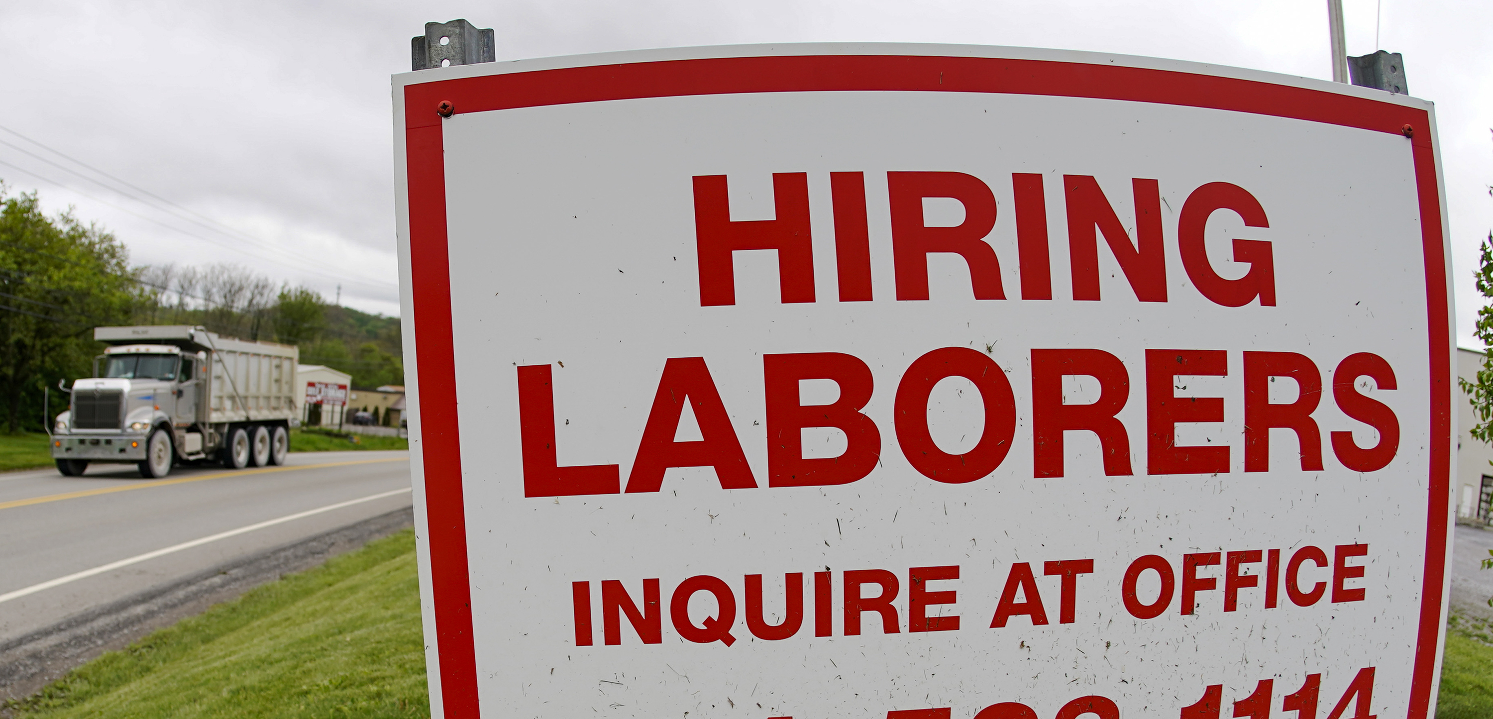 In this file photo from May 5, 2021, a truck passes a sign showing a need to hire laborers outside a concrete products company in Evans City, Pa. Pennsylvania will resume work search requirements in July for hundreds of thousands of people receiving unemployment compensation, a top Wolf administration official said Monday, May 24, 2021. (AP Photo/Keith Srakocic, File)