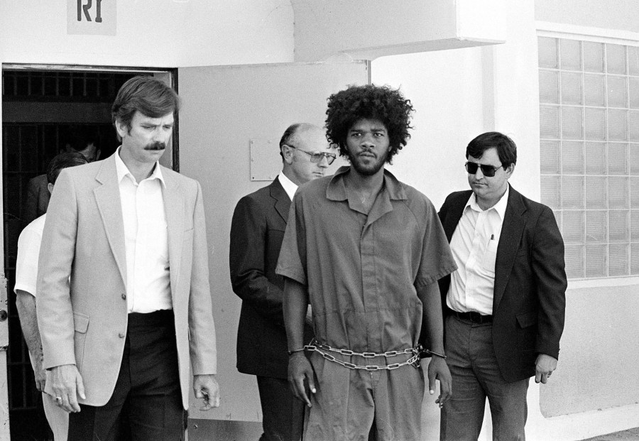 In this July 31, 1983, file photo, Kevin Cooper, center, a suspect in connection with the slashing death of four people in Chino, Calif., is escorted to a car for transport to San Bernardino from Santa Barbara, Calif., after he was arrested by police at Santa Cruz Island. (AP Photo/File)