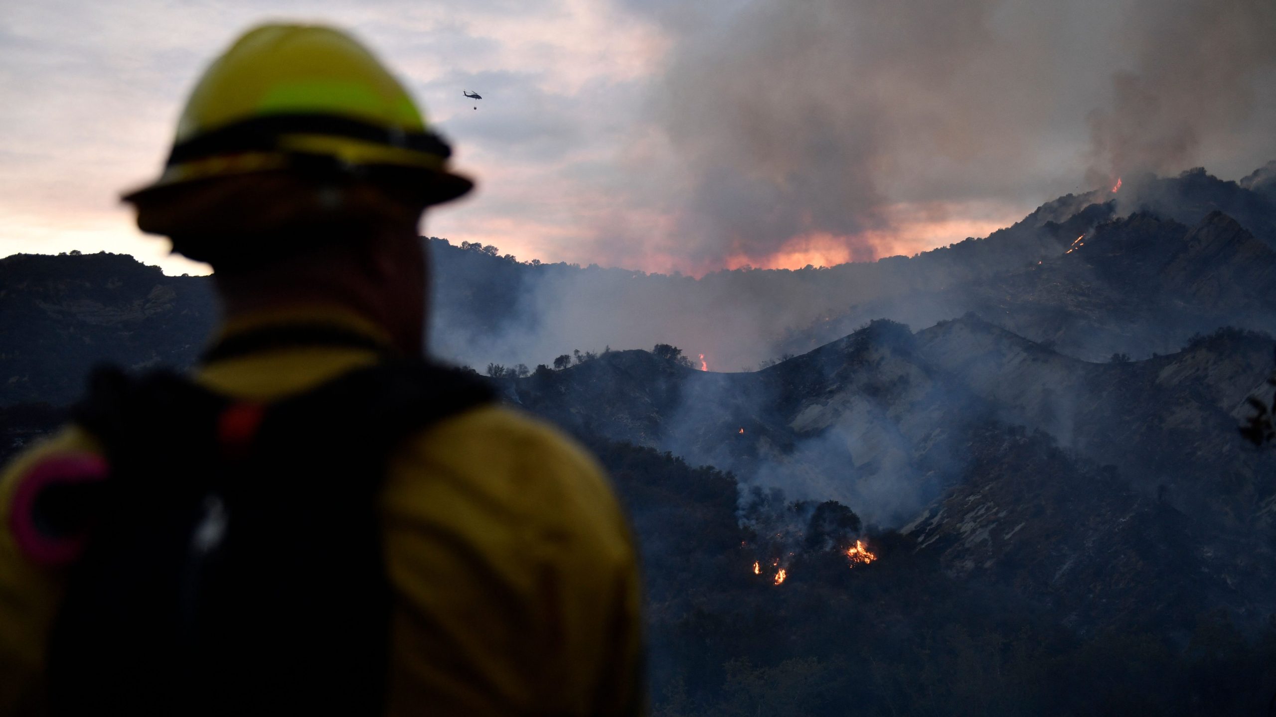 A firefighter watches the flames from the Palisades Fire as helicopters make water drops in the distance in Topanga State Park, northwest of Los Angeles, on May 15, 2021. (PATRICK T. FALLON / AFP / Getty Images)