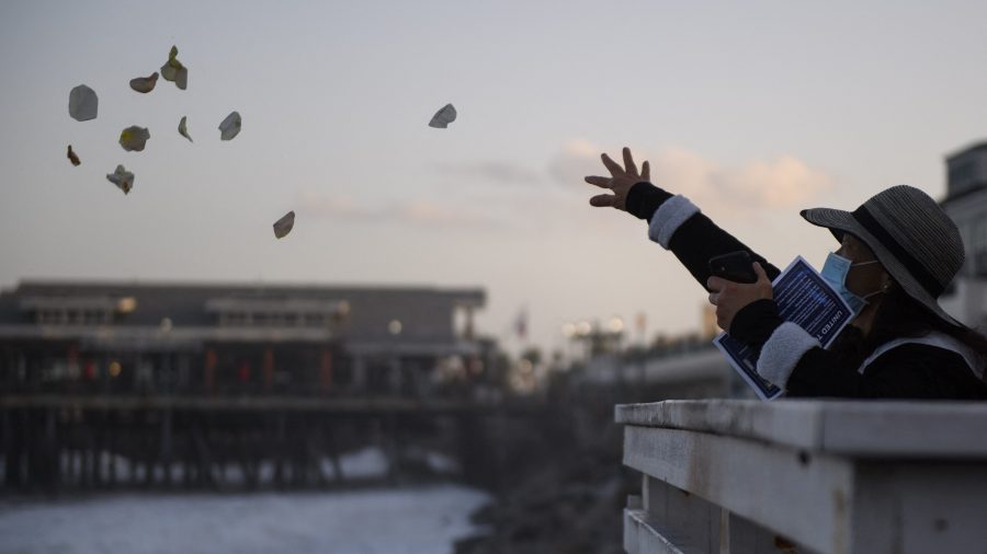 People throw rose petals into the Pacific Ocean during a sunrise vigil organized by United Nurses Associations of California/Union of Health Care Professionals (UNAC/UHCP) at the Redondo Beach Pier on May 22, 2021, to remember health care workers and patients who died from the COVID-19 pandemic. (Patrick T. Fallon / AFP / Getty Images)