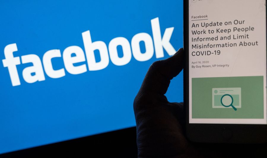 In this photo illustration, a smart phone screen displays a new policy on Covid-19 misinformation with a Facebook website in the background, on May 27, 2021, in Arlington, Virginia - Facebook has reversed its policy banning posts suggesting the Covid-19 was man-made, on the heels of renewed debate over the origins of the virus which first emerged in China. (Photo by ANDREW CABALLERO-REYNOLDS / AFP) (Photo by ANDREW CABALLERO-REYNOLDS/AFP via Getty Images)