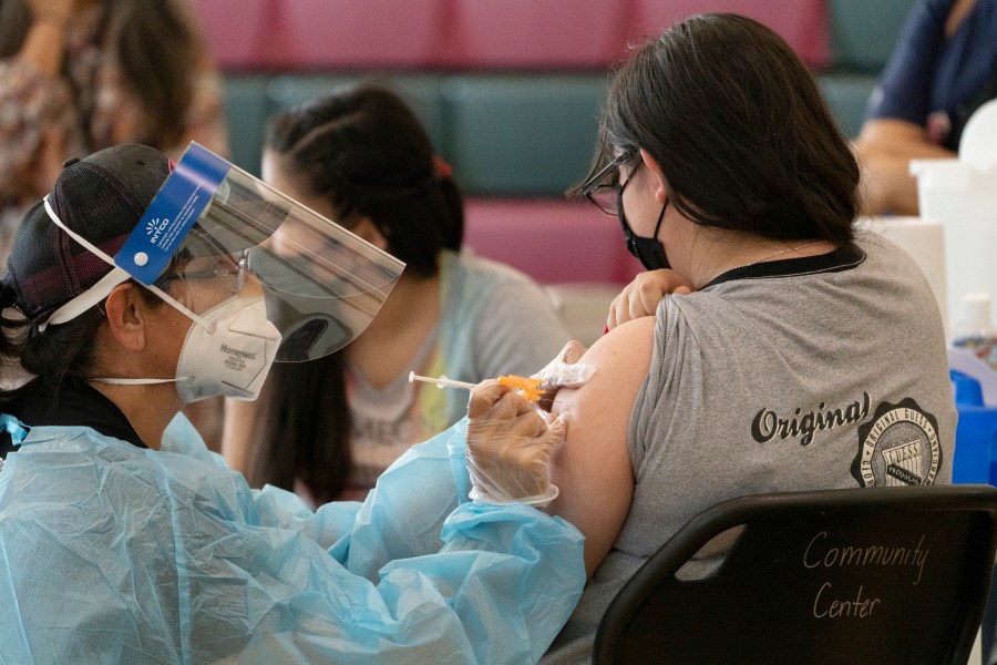 Sisters Guadalupe Flores, 15, right, and Estela Flores, 13, left, from East Los Angeles, get vaccinated with the Pfizer's COVID-19 vaccine by licensed vocational nurse Rita Orozco, far left, at the Esteban E. Torres High School in Los Angeles, Thursday, May 27, 2021. (AP Photo/Damian Dovarganes)