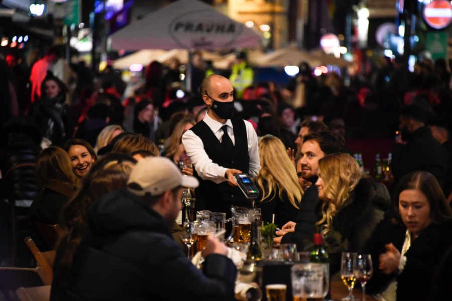 In this Wednesday, Nov. 4, 2020 file photo, a waiter wears a face mask as people eat and drink outside restaurants in Soho, in London. British Prime Minister Boris Johnson is expected to confirm Monday June 14, 2021, that the next planned relaxation of coronavirus restrictions in England will be delayed as a result of the spread of the delta variant first identified in India. (AP Photo/Alberto Pezzali, File)