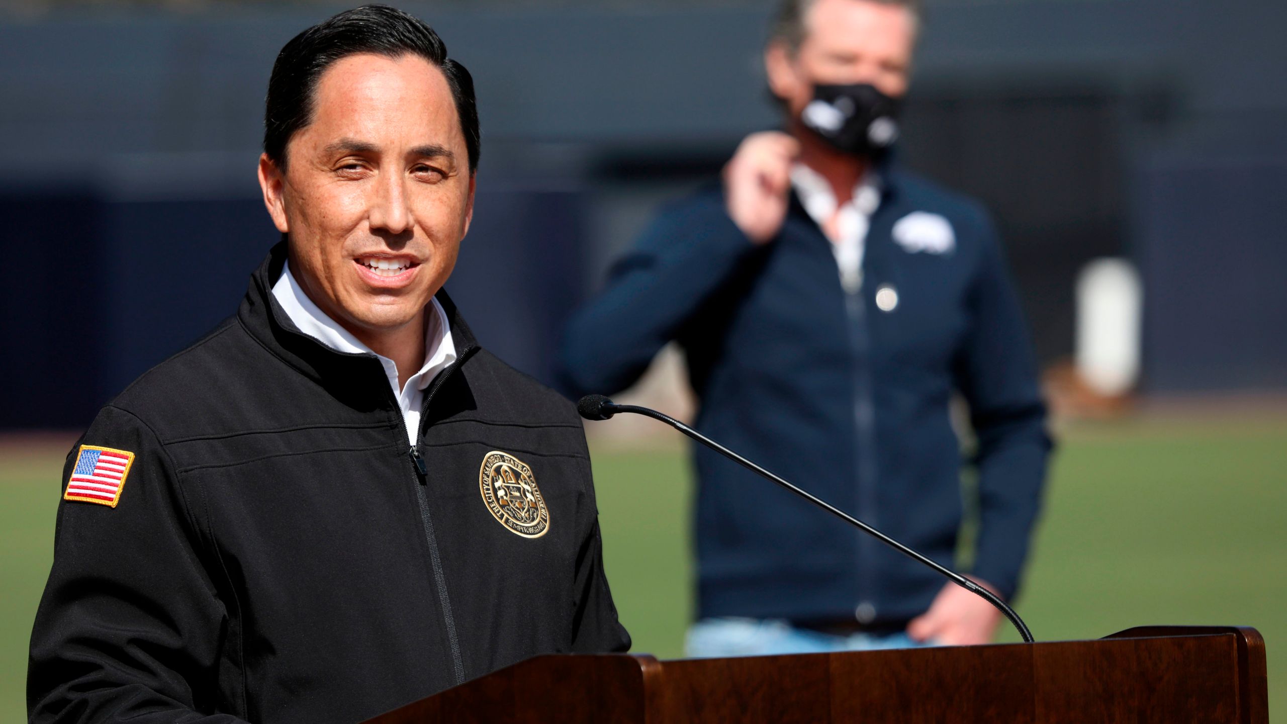 California Governor Gavin Newsom (back) listens as San Diego Mayor Todd Gloria speaks to members of the media during a press conference at Petco Park, February 8, 2021 in San Diego, California, during a visit to the Petco Park Vaccination Supersite. (Sandy Huffaker/POOL/AFP via Getty Images)