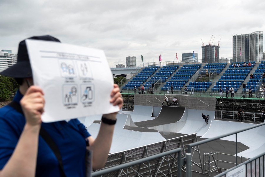 A volunteer holds a poster with measures against covid19 propagation in the BMX freestyle track venue during a test event for the Tokyo 2020 Olympic Games at Ariake Urban Sports Park in Tokyo on May 17, 2021. (CHARLY TRIBALLEAU / AFP)