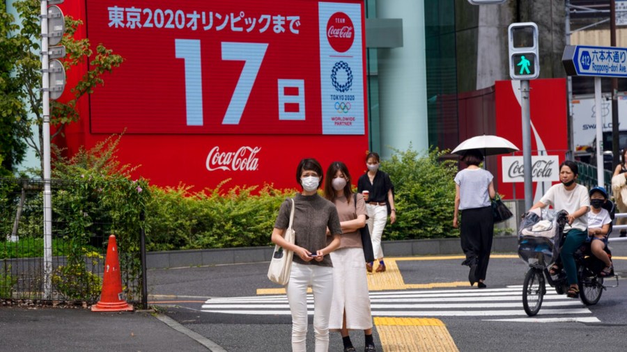 People wearing protective masks wait at a crosswalk as an electric display in the background shows 17 days to Tokyo 2020 Olympics Tuesday, July 6, 2021, in Tokyo. (AP Photo/Kiichiro Sato)