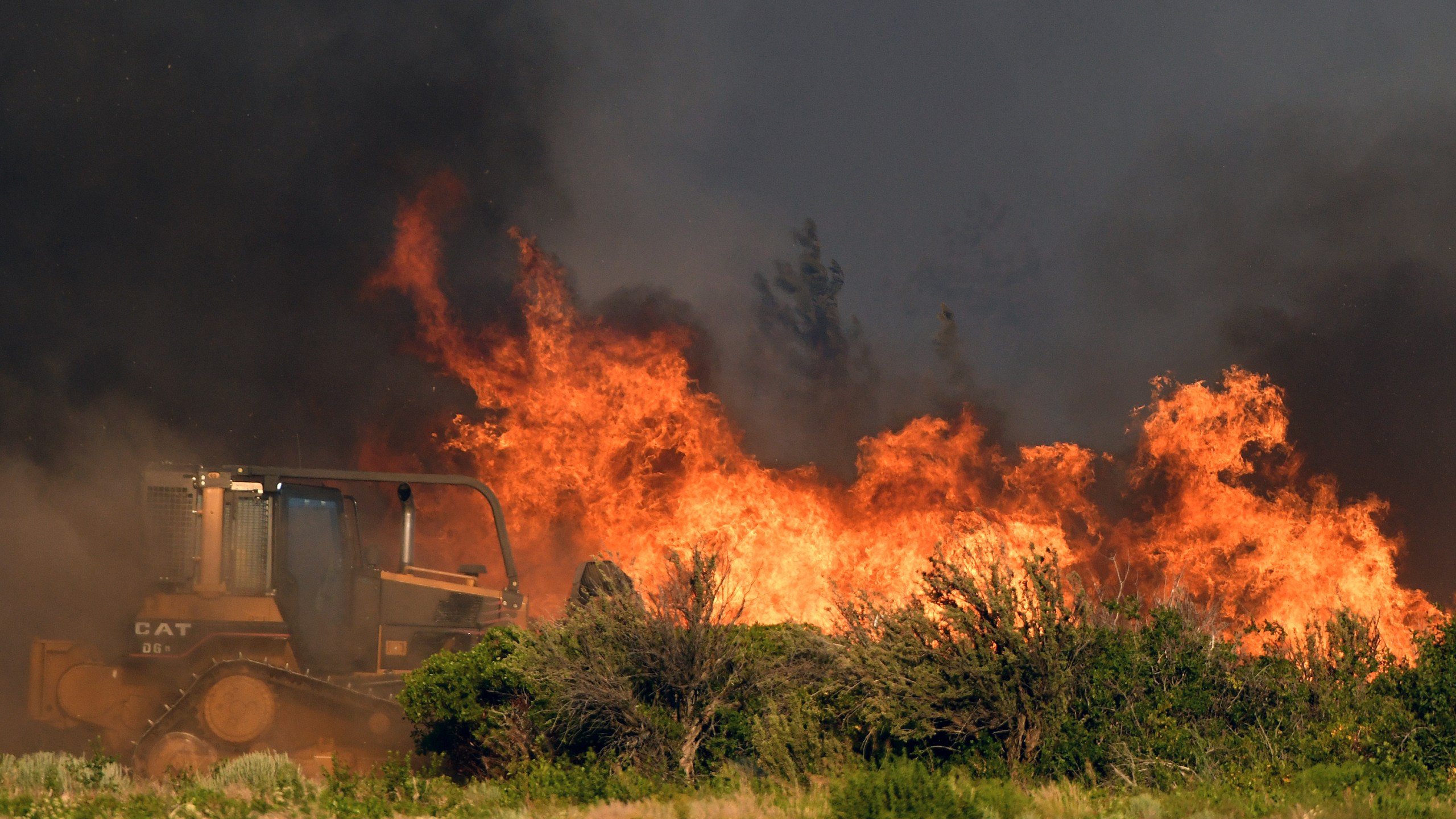 A bulldozer operator works on a fire line as vegetation burns nearby at the Lava Fire on Monday, June 28, 2021, north of Weed, Calif. Officers shot and killed a man who pulled a gun as they tried to keep him out of a complex of marijuana farms in an area of far Northern California where thousands of people have been ordered to evacuate because of a raging wildfire. (Scott Stoddard/Grants Pass Daily Courier via AP)