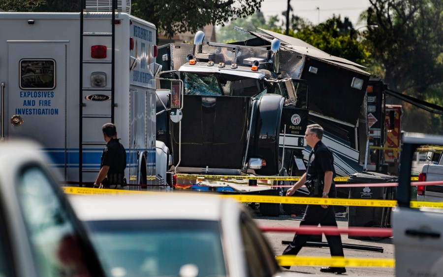 Police officers walk past the remains of an armored Los Angeles Police Department tractor-trailer on July 1, 2021, the morning after illegal fireworks seized at a South Los Angeles home exploded. (Damian Dovarganes / Associated Press)