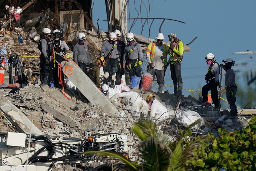 A team works to extricate remains as search and rescue personnel look on, atop the rubble at the Champlain Towers South condo building where scores of people remain missing more than a week after it partially collapsed, Friday, July 2, 2021, in Surfside, Fla. Rescue efforts resumed Thursday evening after being halted for most of the day over concerns about the stability of the remaining structure.(AP Photo/Mark Humphrey)