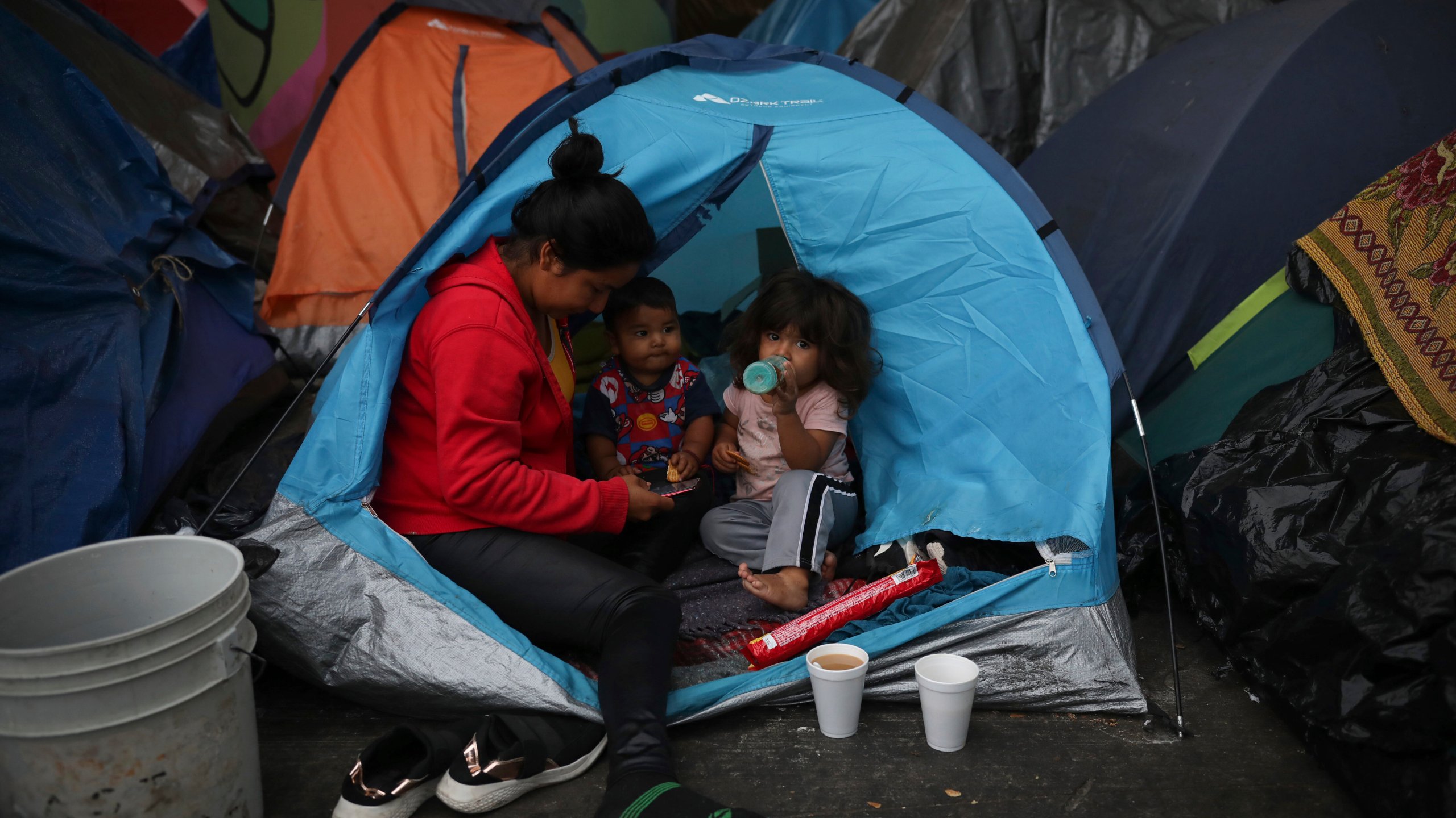 Mexican Amary Martinez, and her children, Jason and Itzel, sit on the edge of their tent at a migrant camp near El Chaparral pedestrian border bridge in Tijuana, Mexico, Friday, July 2, 2021. The migrant camp of about 2,000 asylum-seekers, mostly families, blocks a pedestrian entrance to the US border crossing with San Diego. Mexican officials have suggested they will try to relocate them in coming days in anticipation that the two governments could agree to reopen the border to non-essential travel in the coming weeks. (AP Photo/Emilio Espejel)