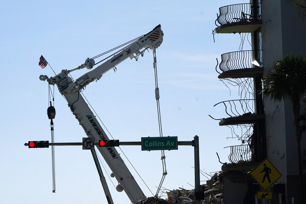 An American flag flies from a crane next to the Champlain Towers South condo building, where scores of victims remain missing more than a week after it partially collapsed, Sunday, July 4, 2021, in Surfside, Fla. (AP Photo/Lynne Sladky)