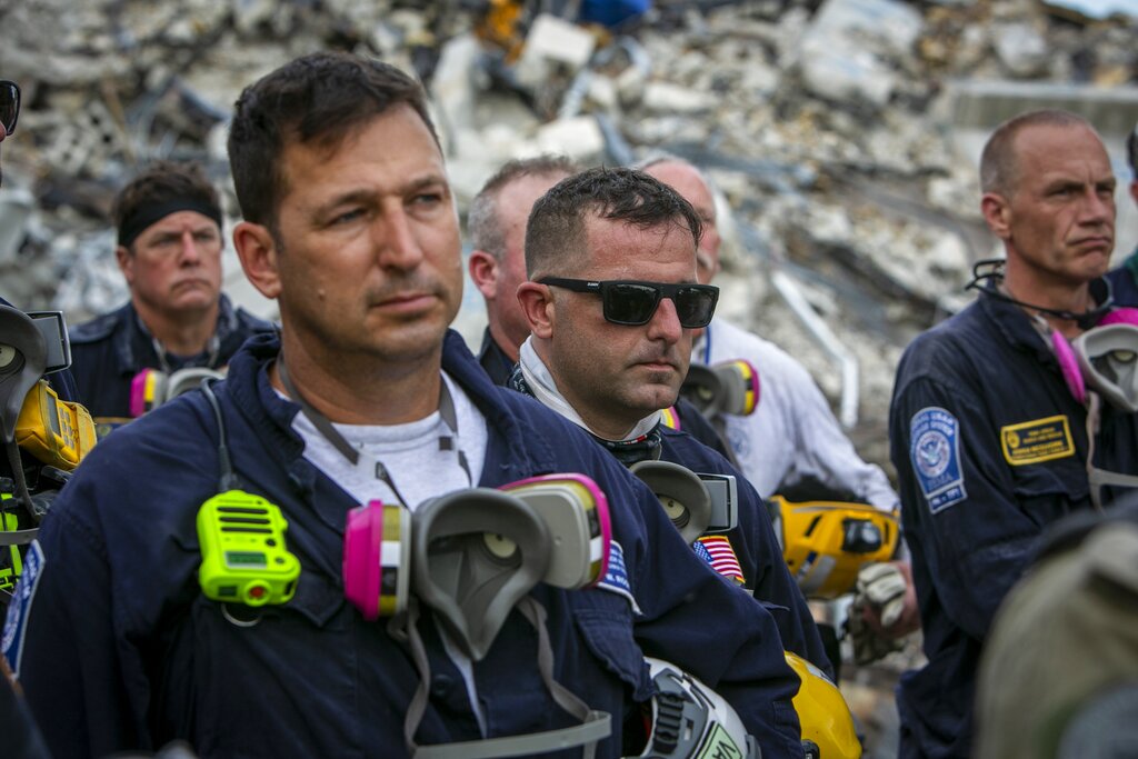 Members of a search and rescue team stand in front of the rubble that once was Champlain Towers South during a prayer ceremony in Surfside, Fla., Wednesday, July 7, 2021. (Jose A Iglesias/Miami Herald via AP)