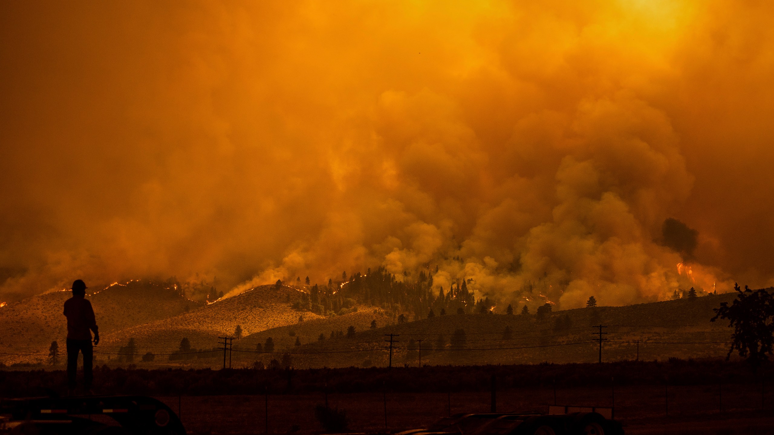 A truck driver who hauls fire equipment watches as the Sugar Fire, part of the Beckwourth Complex Fire, burns in Doyle, Calif., on Saturday, July 10, 2021. (AP Photo/Noah Berger)