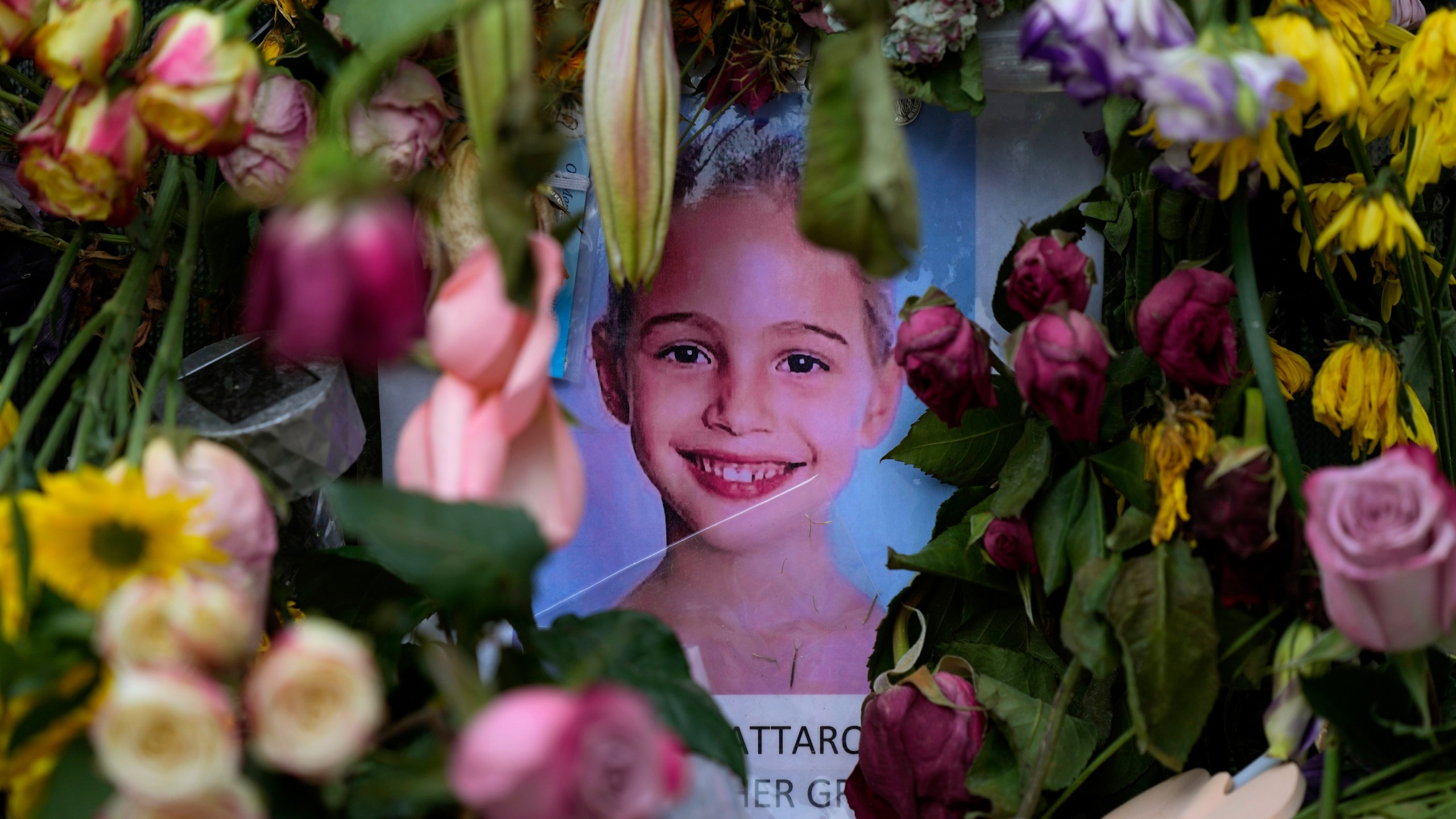 Flowers from well-wishers surround a photograph of Stella Cattarossi, age 7, on a makeshift memorial wall for the victims of the Champlain Towers South building collapse, on Monday, July 12, 2021, in Surfside, Fla. (AP Photo/Rebecca Blackwell)