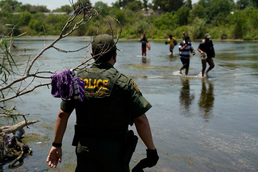 In this June 15, 2021, file photo, a Border Patrol agent watches as a group of migrants walk across the Rio Grande on their way to turning themselves in upon crossing the U.S.-Mexico border in Del Rio, Texas. A Justice Department attorney says the U.S. Centers for Disease Control and Prevention will issue an order this week about treatment of children under a public health order that has prevented migrants from seeking asylum at U.S. borders. (AP Photo/Eric Gay, File)