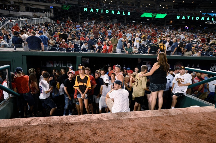 Spectators stand in the visiting team dugout during a stoppage in play due to an incident near the ballpark in the sixth inning of a baseball game between the Washington Nationals and the San Diego Padres, Saturday, July 17, 2021, in Washington. (AP Photo/Nick Wass)