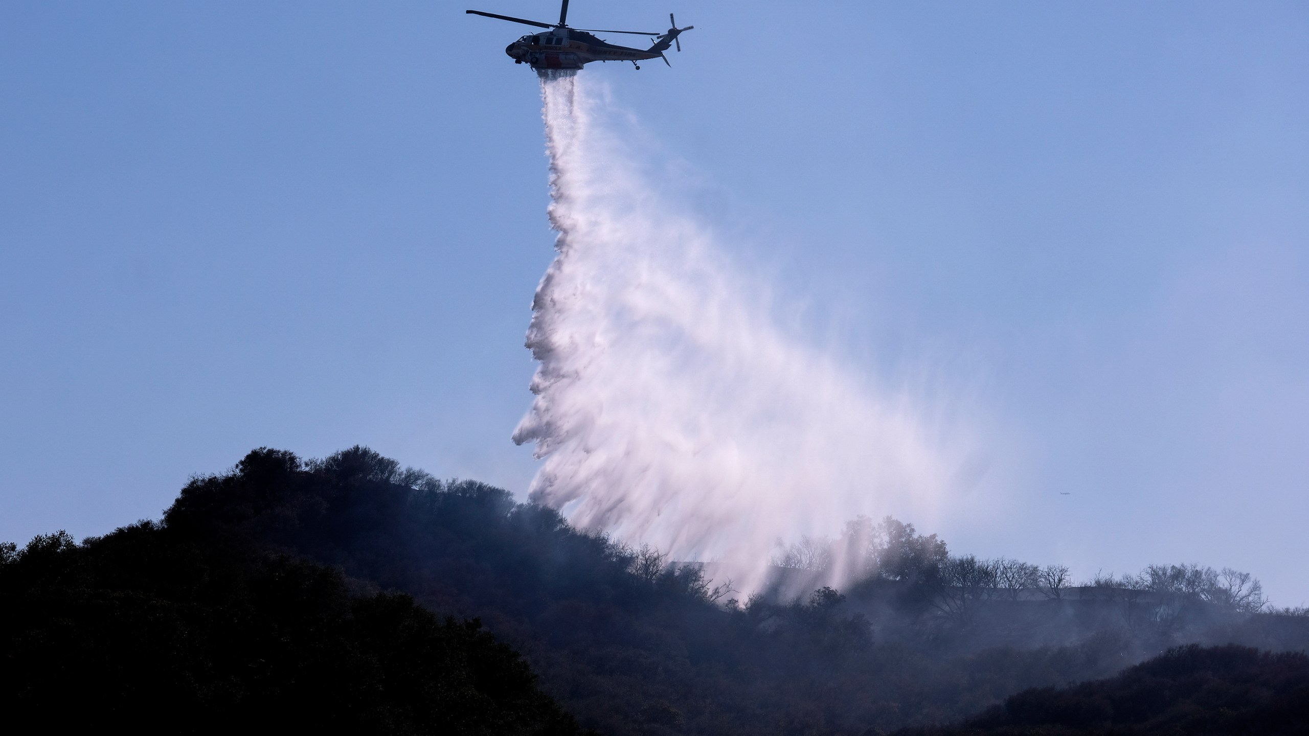 A helicopter makes a water drop to put out hotspots in a wildfire in Topanga, west of Los Angeles, Monday, July 19, 2021. (AP Photo/Ringo H.W. Chiu)