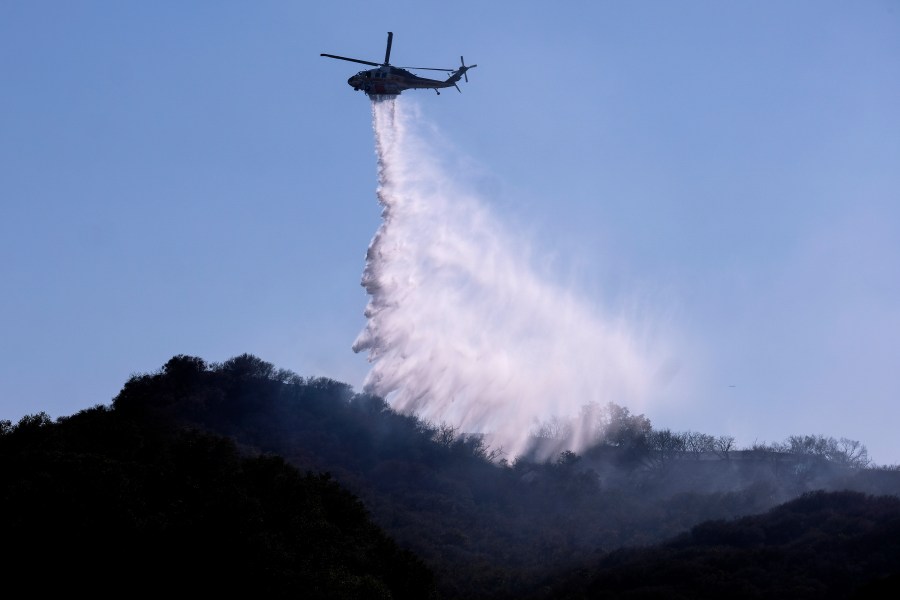 A helicopter makes a water drop to put out hotspots in a wildfire in Topanga, west of Los Angeles, Monday, July 19, 2021. (AP Photo/Ringo H.W. Chiu)