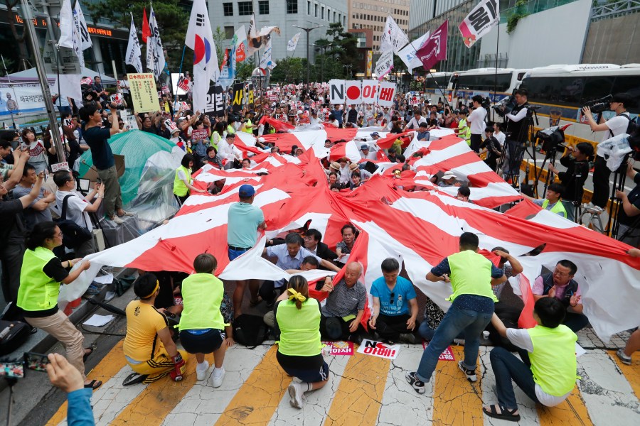 In this July 20, 2019, file photo, protesters tear a Japanese rising sun flag during a rally denouncing the Japanese government's decision on their exports to South Korea in front of Japanese Embassy in Seoul, South Korea. Japan’s “rising sun” flag is raising anger at the Olympics, with some of the host nation’s neighbors calling for it to be banned during the Tokyo Games, which start Friday, July 23, 2021. (AP Photo/Ahn Young-joon, File)