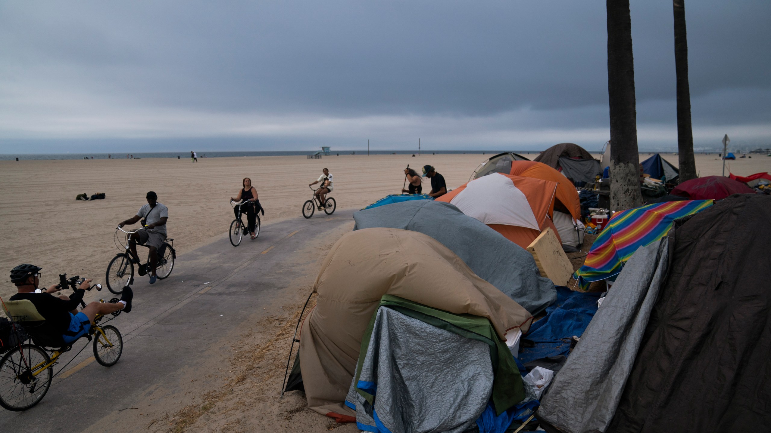 People ride their bikes past a homeless encampment set up along the boardwalk in the Venice neighborhood of Los Angeles, Tuesday, June 29, 2021. The proliferation of homeless encampments on Venice Beach has sparked an outcry from residents and created a political spat among Los Angeles leaders. (AP Photo/Jae C. Hong)