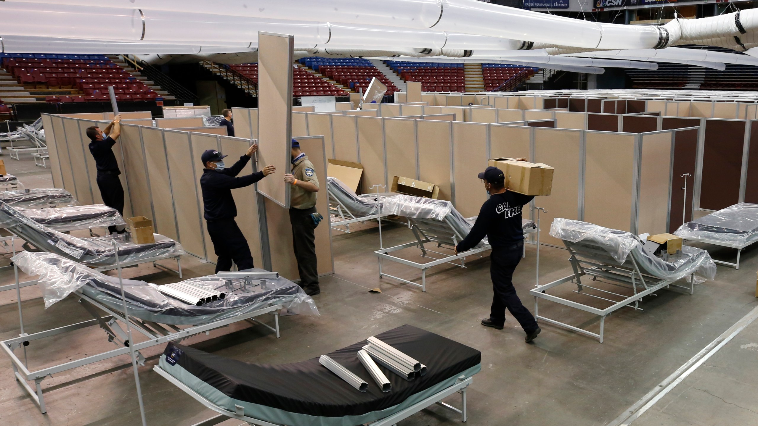 In this April 18, 2020 file photo partitions are installed between beds as work is performed to turn the Sleep Train Arena into a 400 bed emergency field hospital to help deal with the coronavirus, in Sacramento, Calif. (AP Photo/Rich Pedroncelli, File)