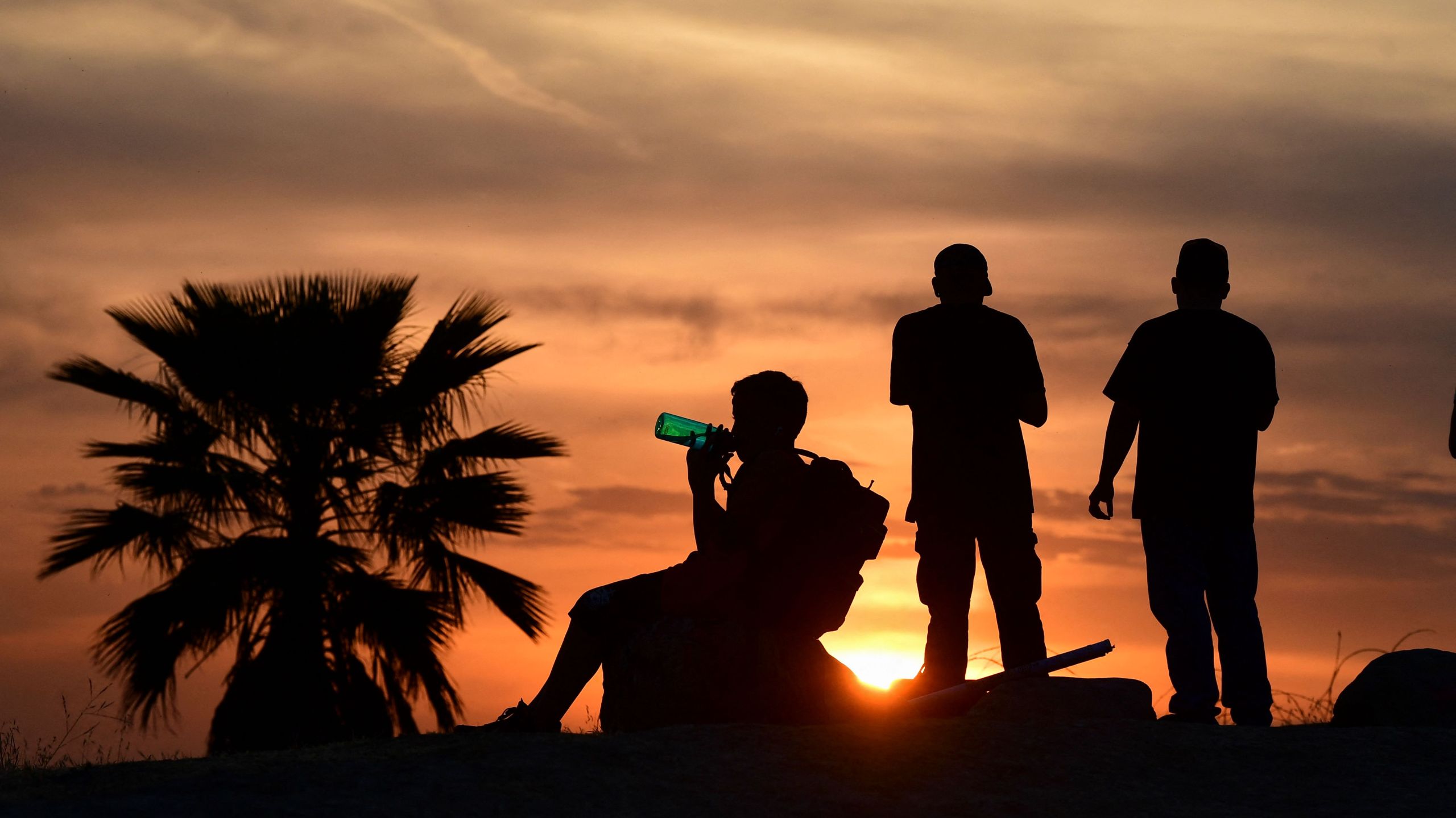 People view the sun set as a child drinks from a water bottle on June 15, 2021 in Los Angeles, as temperatures soar in an early-season heatwave. (Frederic J. BROWN/AFP via Getty Images)