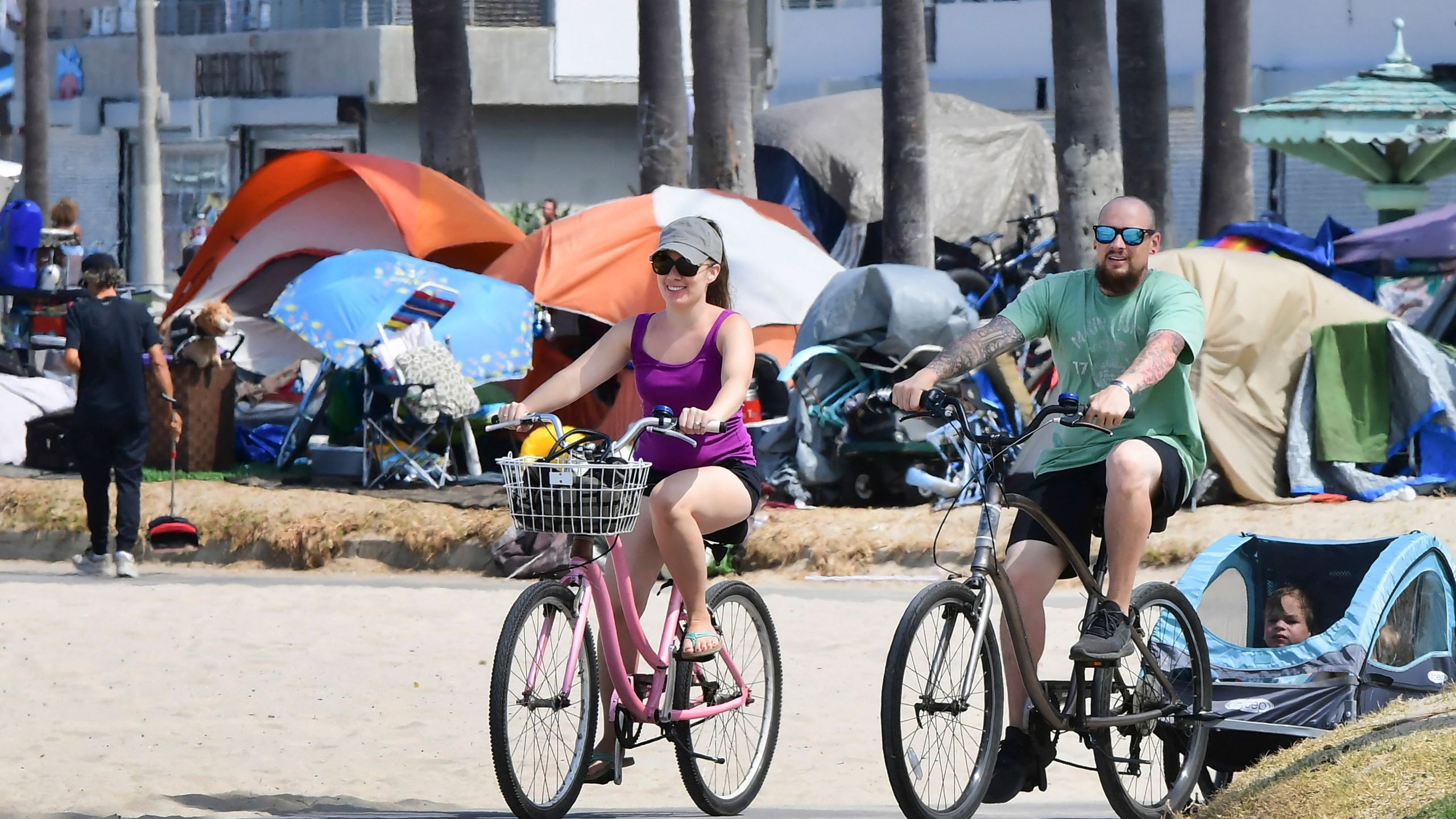 Cyclists ride past tents housing the homeless along the Ocean Front Walk in Venice, California on June 30, 2021, where an initiative began this week offering people in homeless encampments a voluntary path to permanent housing. (Frederic J. Brown AFP via Getty Images)