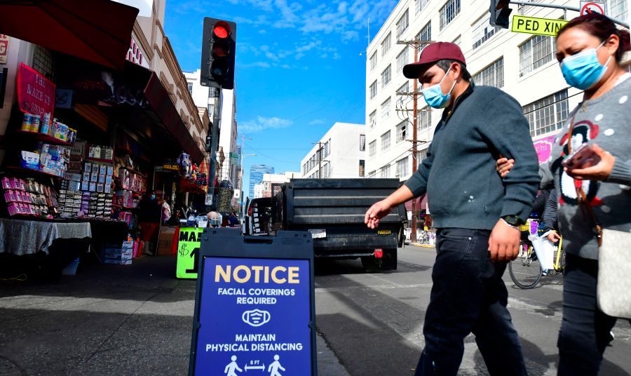 A signboard reminds people of the face covering requirement as pedestrians wear facemasks due to the coronavirus in Los Angeles on Nov. 12, 2020. (Frederic J. Brown/AFP via Getty Images)