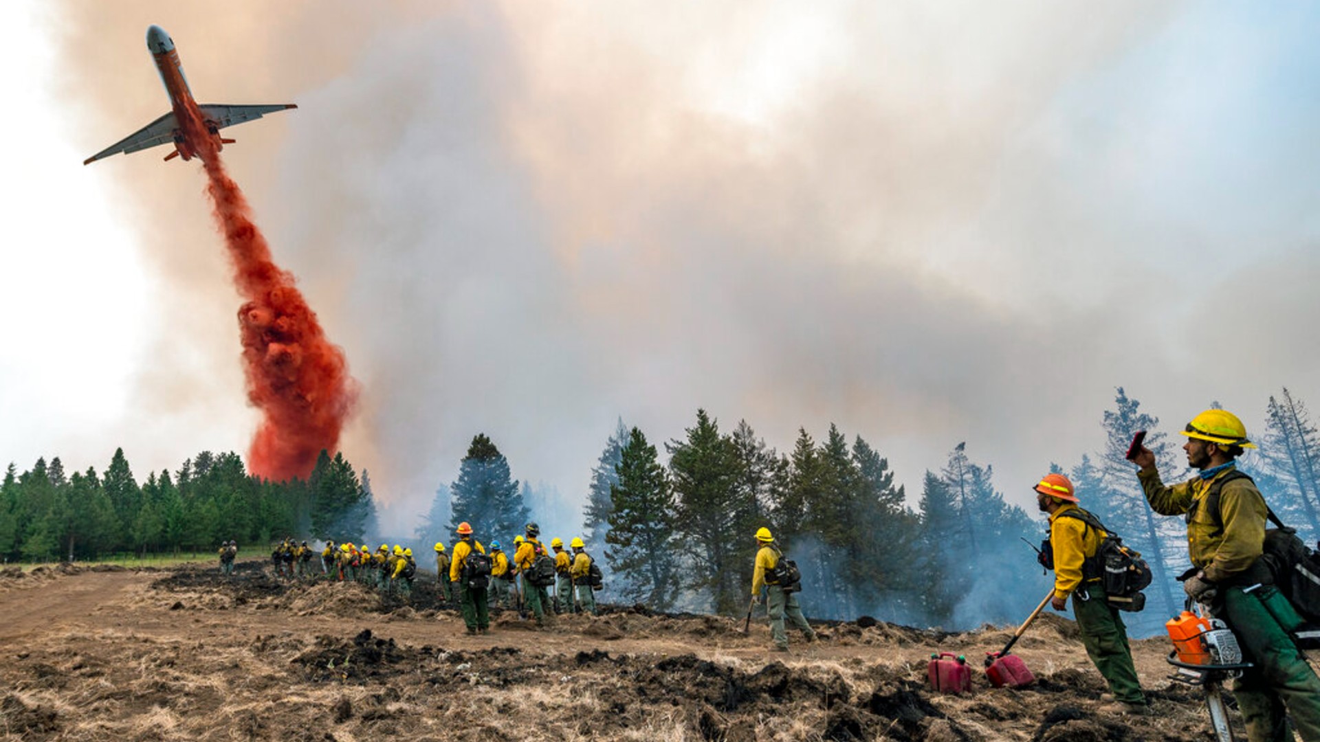 Wildland firefighters watch and take video with their cellphones as a plane drops fire retardant on Harlow Ridge above the Lick Creek Fire, southwest of Asotin, Wash., Monday, July 12, 2021. (Pete Caster/Lewiston Tribune via AP)