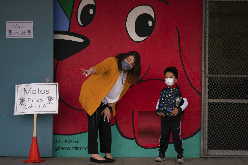 Kindergarten teacher Lilia Matos and her student Jesus Mendez stand outside their classroom on the first day of in-person learning at Heliotrope Avenue Elementary School in Maywood, Calif., Tuesday, April 13, 2021. (AP Photo/Jae C. Hong)