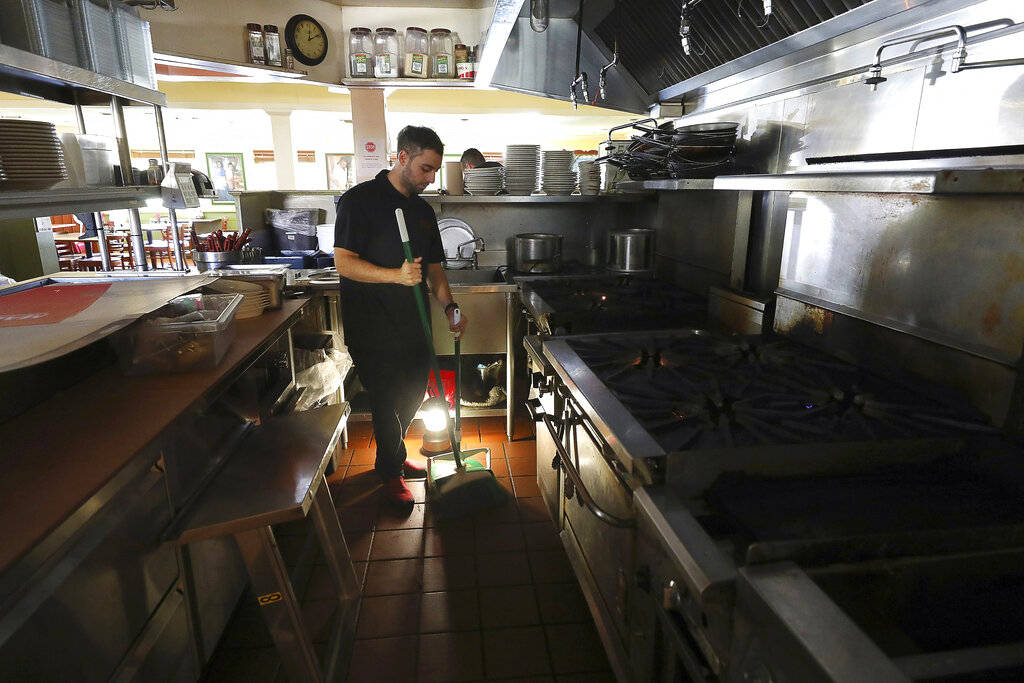 In this Oct. 10, 2019, file photo, Salvador Espinosa sweeps in the kitchen of a Mary's Pizza Shack restaurant during a Pacific Gas & Electric power shutdown in Santa Rosa, Calif. (Christopher Chung//The Press Democrat via AP, FIle)