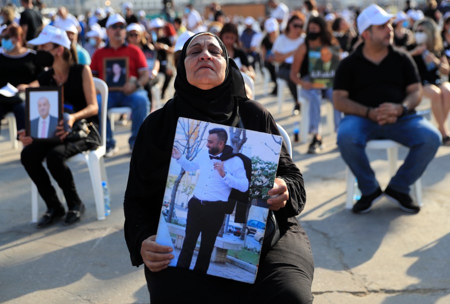 The mother of a victim who was killed in the massive blast last year at the Beirut port holds a portrait of her son as she attends a Mass held to commemorate the first year anniversary of the deadly blast, at the Beirut port in Lebanon on Aug. 4, 2021. United in grief and anger, families of the victims and other Lebanese came out into the streets of Beirut on Wednesday to demand accountability as banks, businesses and government offices shuttered to mark one year since the horrific explosion. (AP Photo/Hussein Malla)