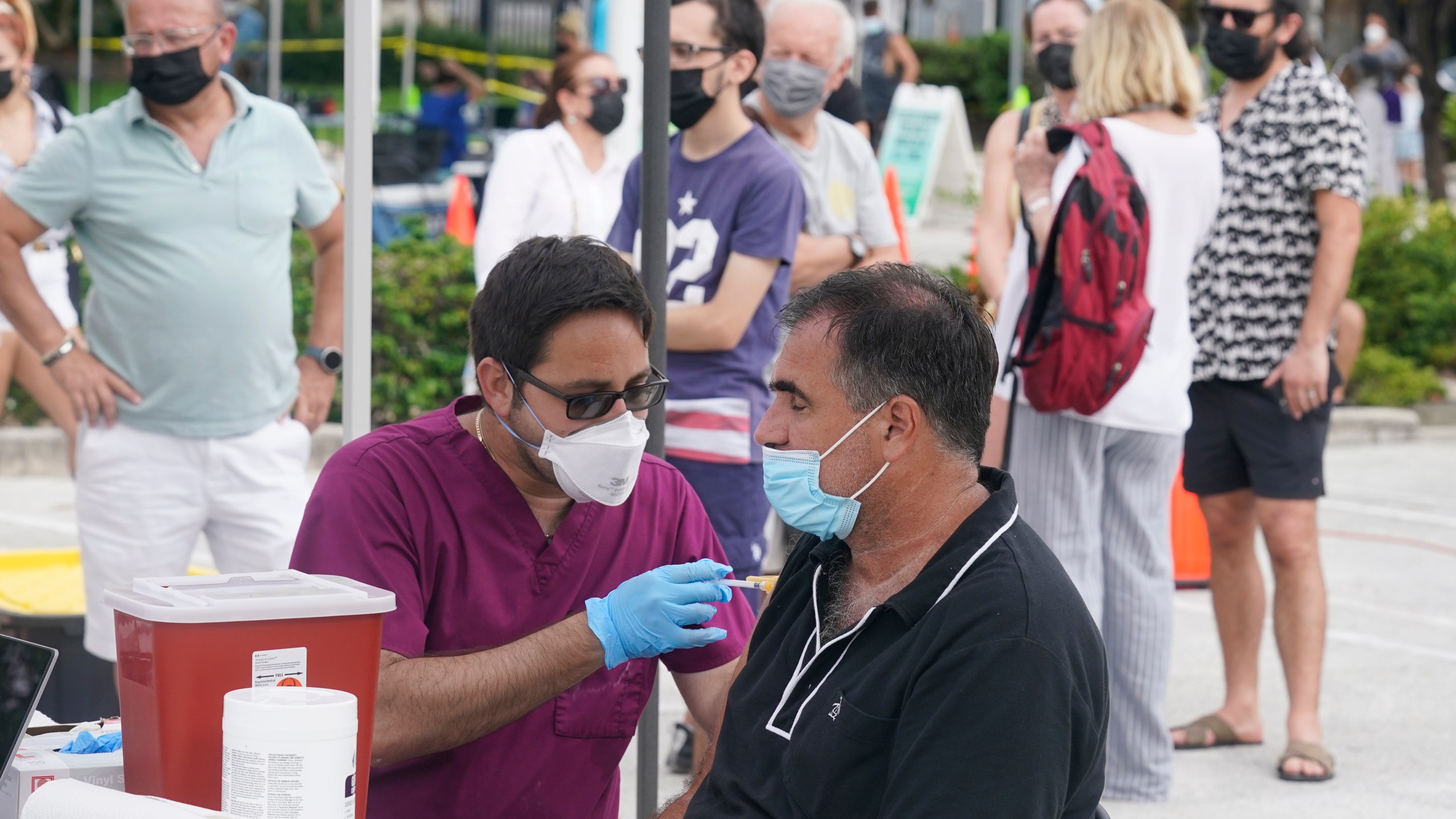 Carlos Anacleto closes his eyes as he receives the Pfizer COVID-19 vaccine from nurse Jorge Tase, as others wait their turn, Wednesday, Aug. 4, 2021, in Miami Beach, Fla. (AP Photo/Marta Lavandier)