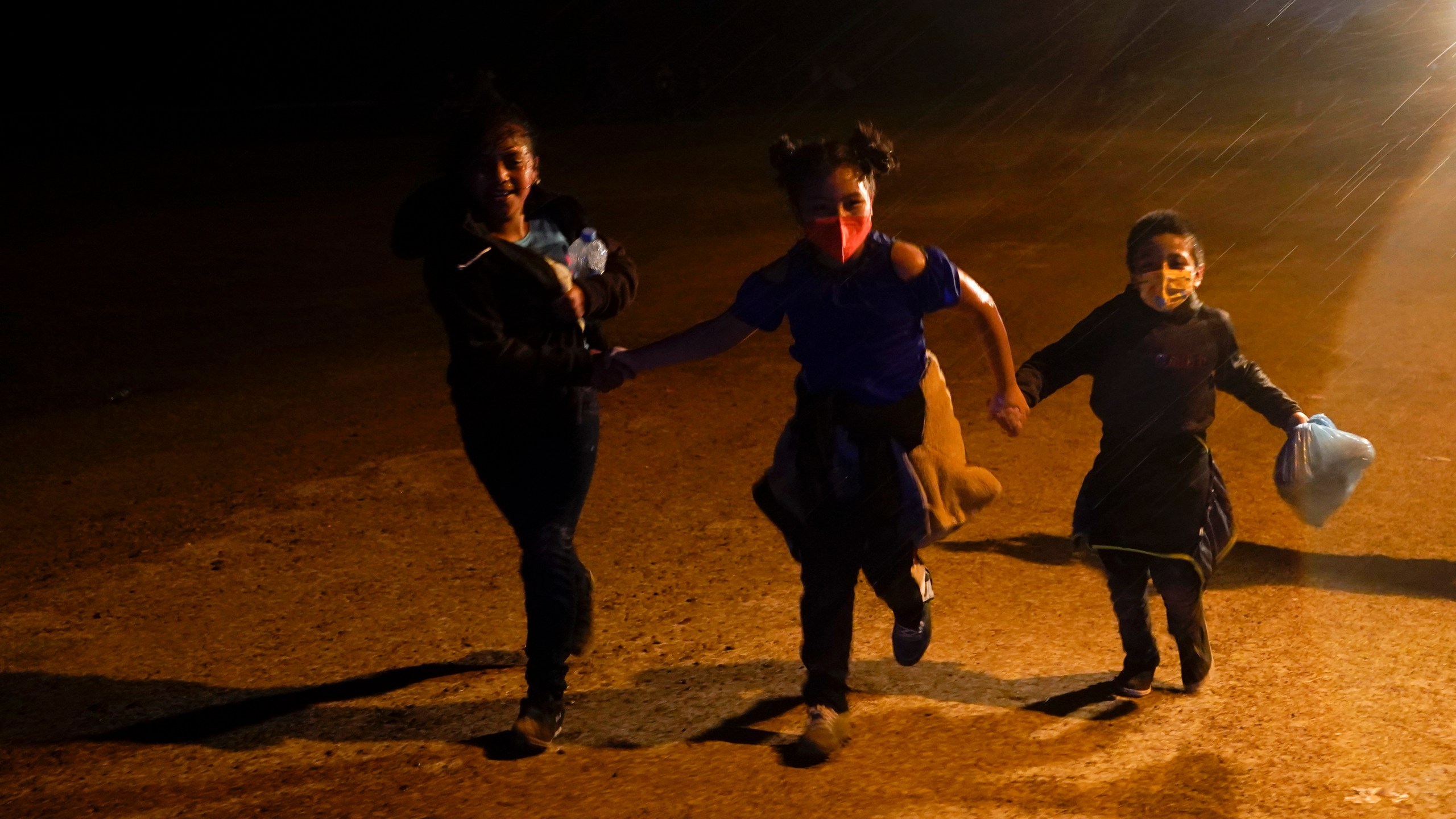 In this May 11, 2021 file photo three young migrants hold hands as they run in the rain at an intake area after turning themselves in upon crossing the U.S.-Mexico border in Roma, Texas. An official says the Biden administration has begun flying some Central American families deep into Mexico as authorities encounter more families and unaccompanied children at the U.S.-Mexico border. (AP Photo/Gregory Bull, File)