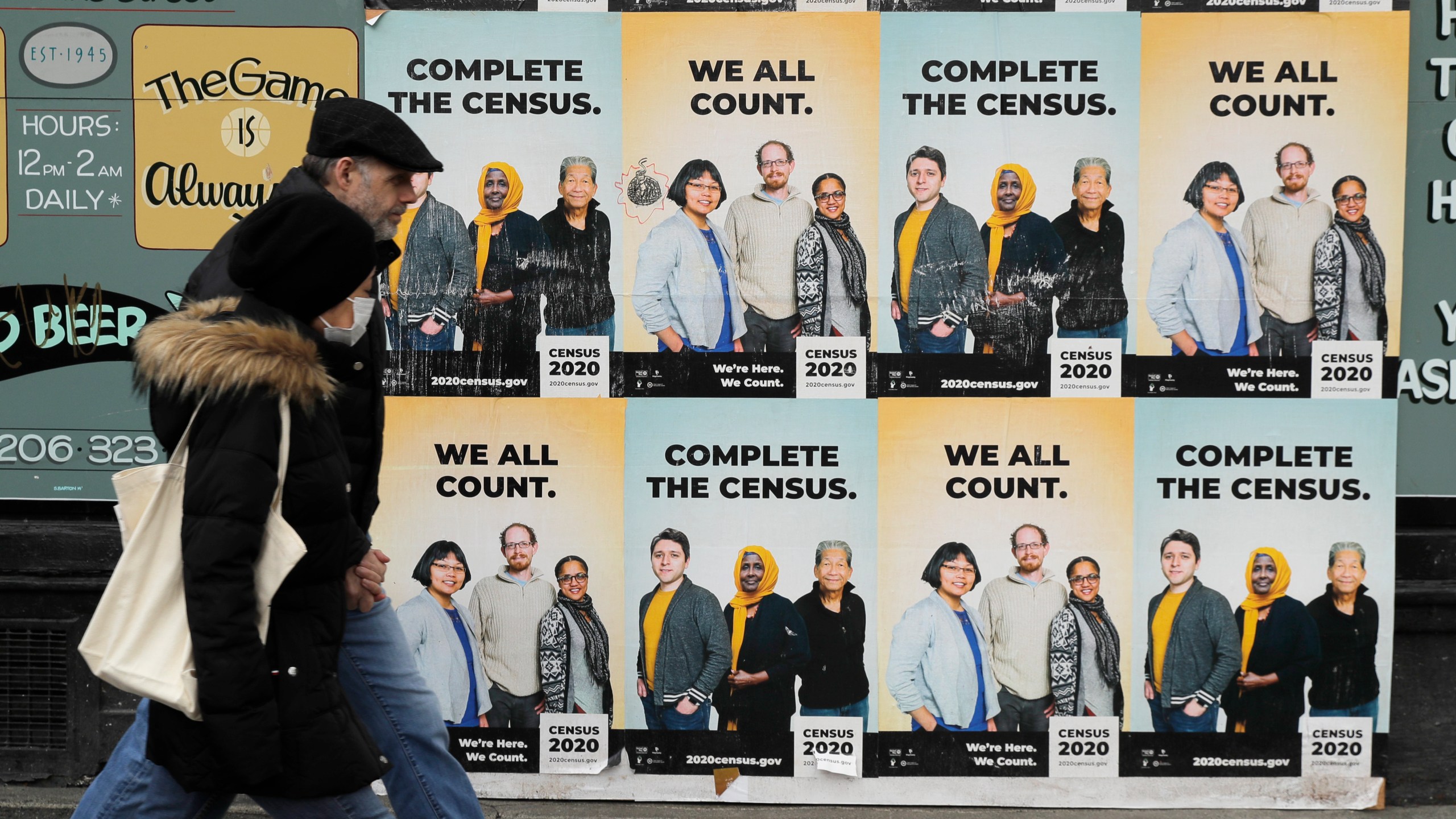 In this Wednesday, April 1, 2020 file photo, People walk past posters encouraging participation in the 2020 Census in Seattle's Capitol Hill neighborhood. From McKenzie County, North Dakota to St. Johns County Florida, the growth in the number of people who identified as multiracial on 2020 census responses soared over the last decade, rising from under 3% to more than 10% of the U.S. population from 2010 and 2020.(AP Photo/Ted S. Warren, File)