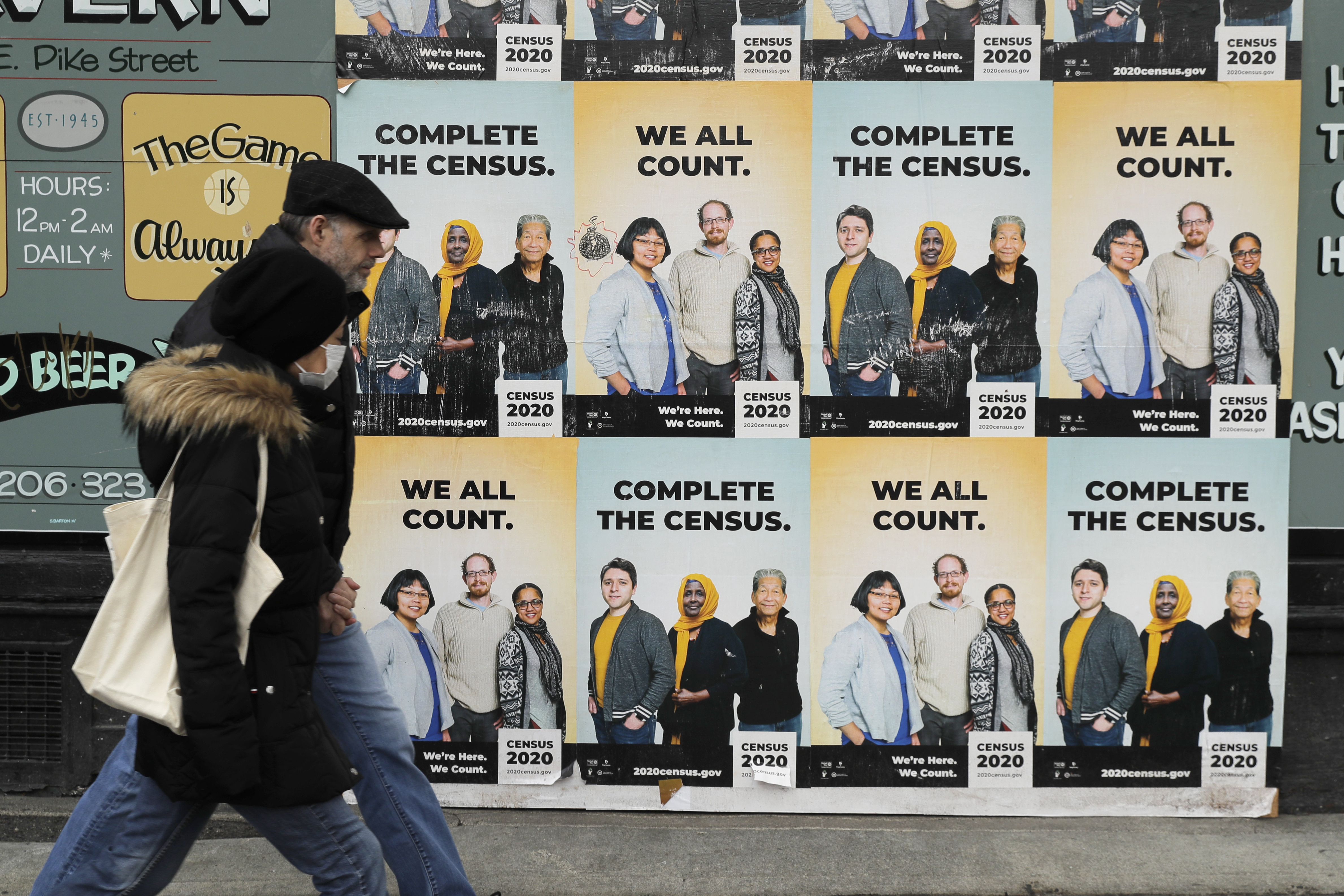 In this Wednesday, April 1, 2020 file photo, People walk past posters encouraging participation in the 2020 Census in Seattle's Capitol Hill neighborhood. From McKenzie County, North Dakota to St. Johns County Florida, the growth in the number of people who identified as multiracial on 2020 census responses soared over the last decade, rising from under 3% to more than 10% of the U.S. population from 2010 and 2020.(AP Photo/Ted S. Warren, File)