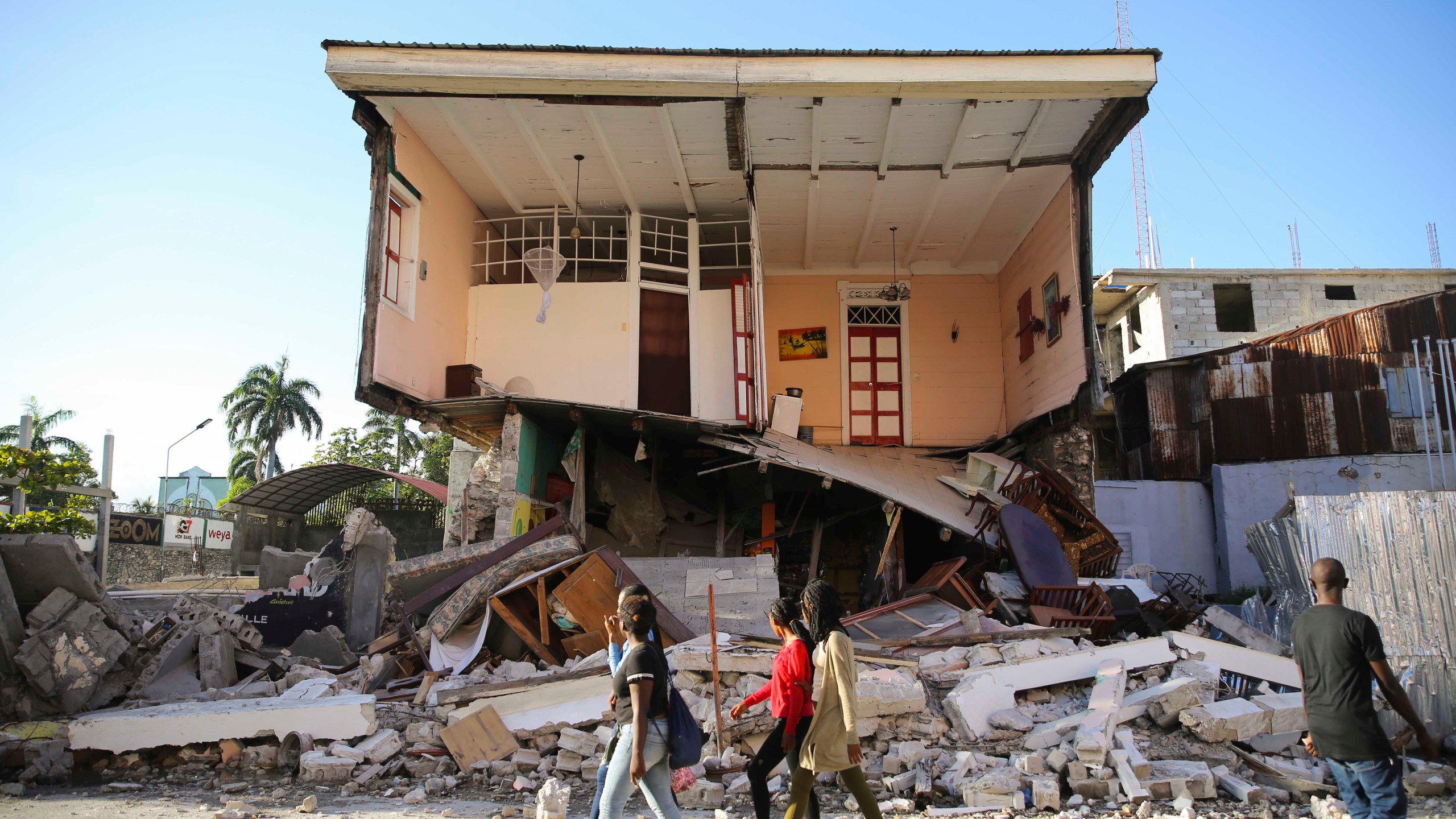 People walk past a home destroyed by the earthquake in Les Cayes, Haiti, Saturday, Aug. 14, 2021. A 7.2 magnitude earthquake struck Haiti on Saturday, with the epicenter about 125 kilometers (78 miles) west of the capital of Port- au-Prince, the US Geological Survey said. (AP Photo/Joseph Odelyn)