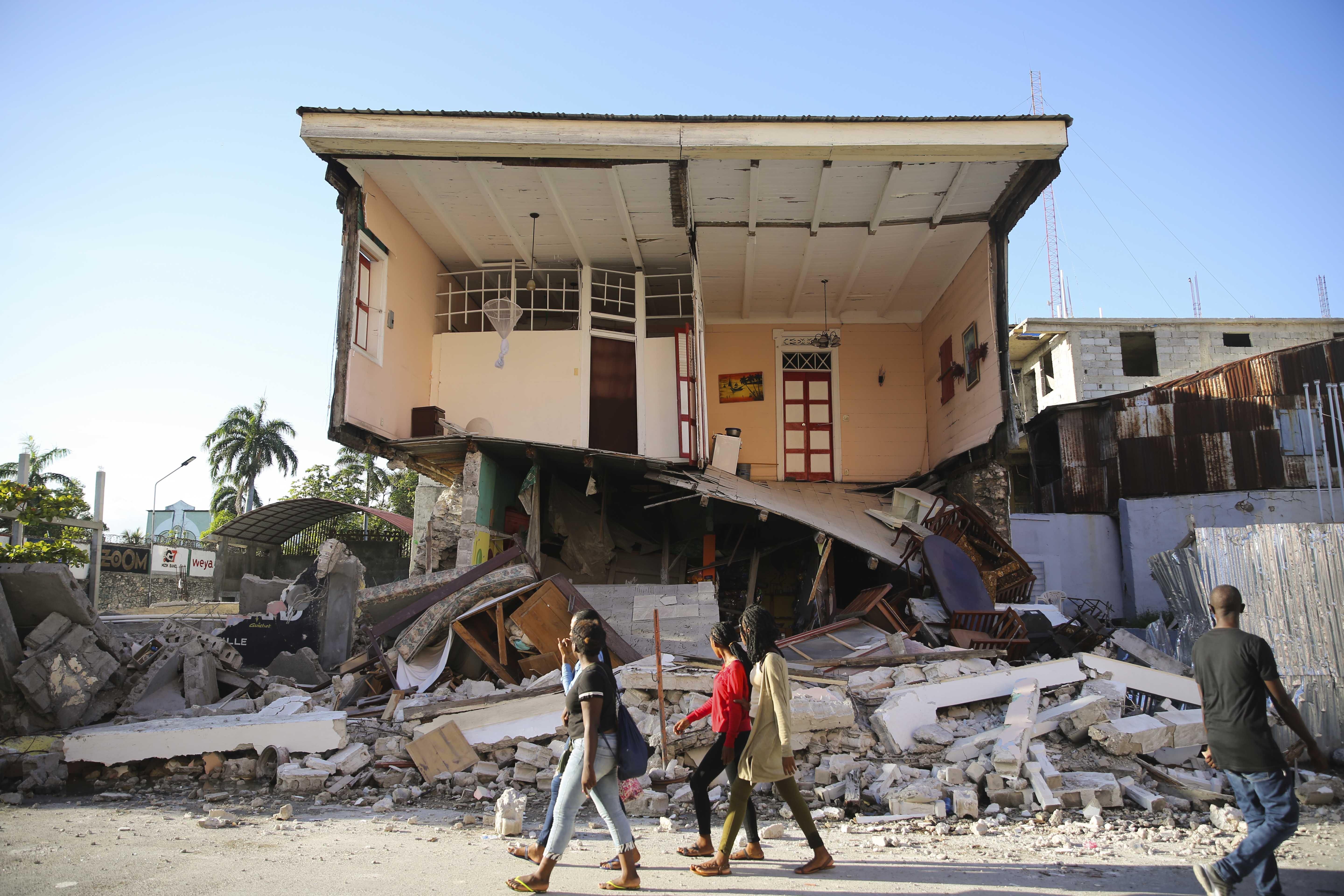 People walk past a home destroyed by the earthquake in Les Cayes, Haiti, Saturday, Aug. 14, 2021. A 7.2 magnitude earthquake struck Haiti on Saturday, with the epicenter about 125 kilometers (78 miles) west of the capital of Port- au-Prince, the US Geological Survey said. (AP Photo/Joseph Odelyn)