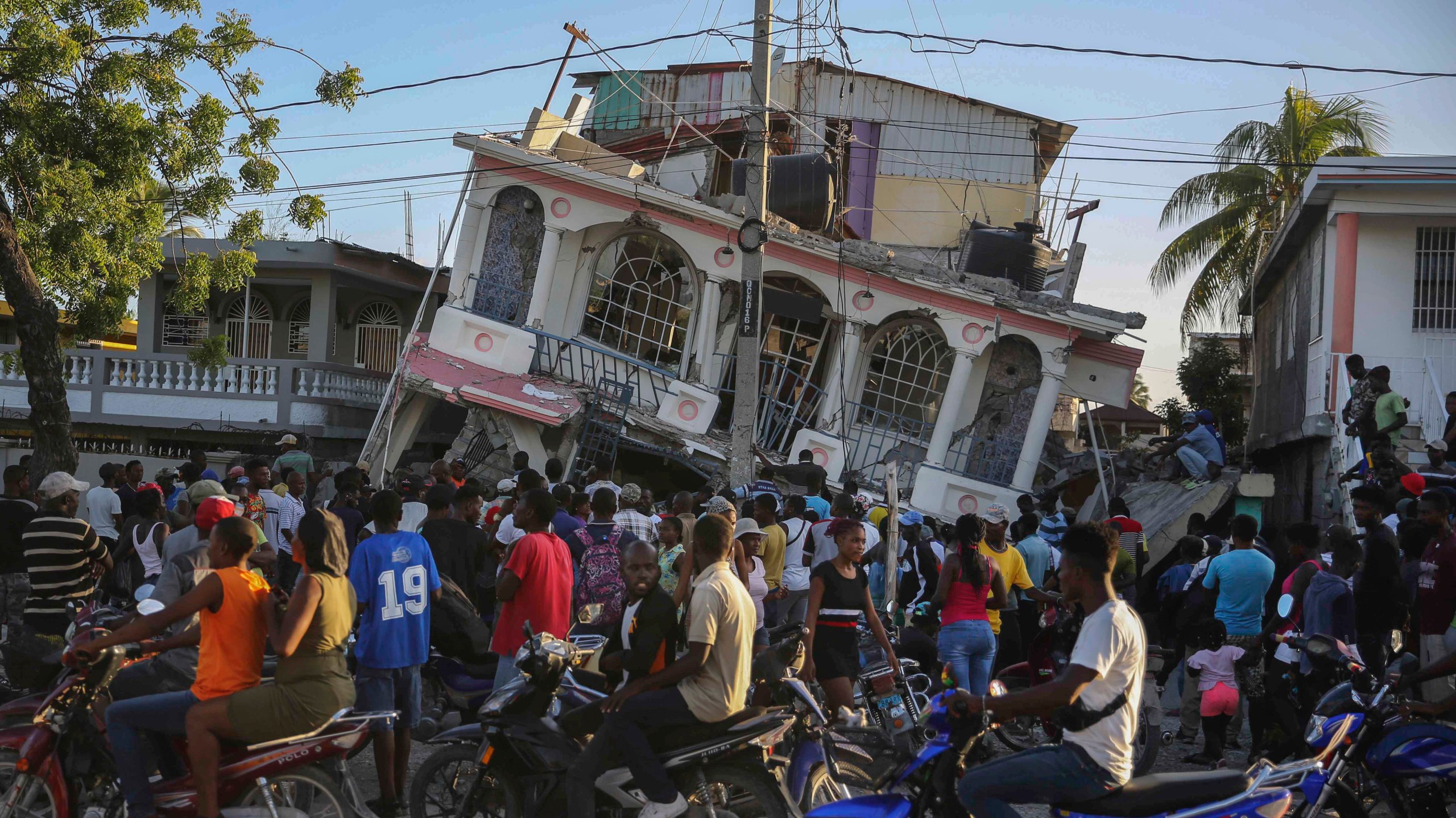 People gather outside the Petit Pas Hotel, destroyed by the earthquake in Les Cayes, Haiti, Saturday, Aug. 14, 2021. A 7.2 magnitude earthquake struck Haiti on Saturday, with the epicenter about 125 kilometers (78 miles) west of the capital of Port-au-Prince, the US Geological Survey said. (AP Photo/Joseph Odelyn)