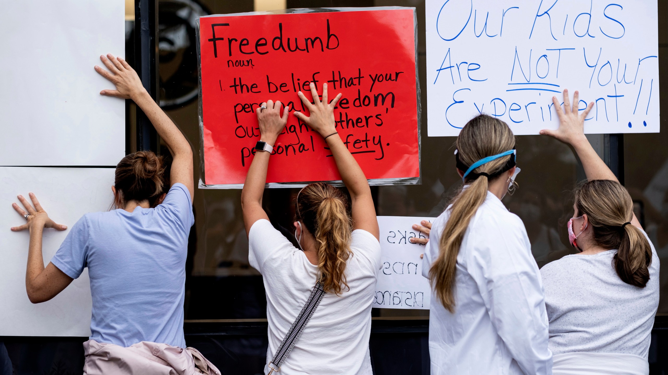 People in favor of a mask mandate for Cobb County schools hold signs against the window to the office during the school board meeting Thursday, Aug. 19, 2021, in Marietta, Ga. (Ben Gray/Atlanta Journal-Constitution via AP)