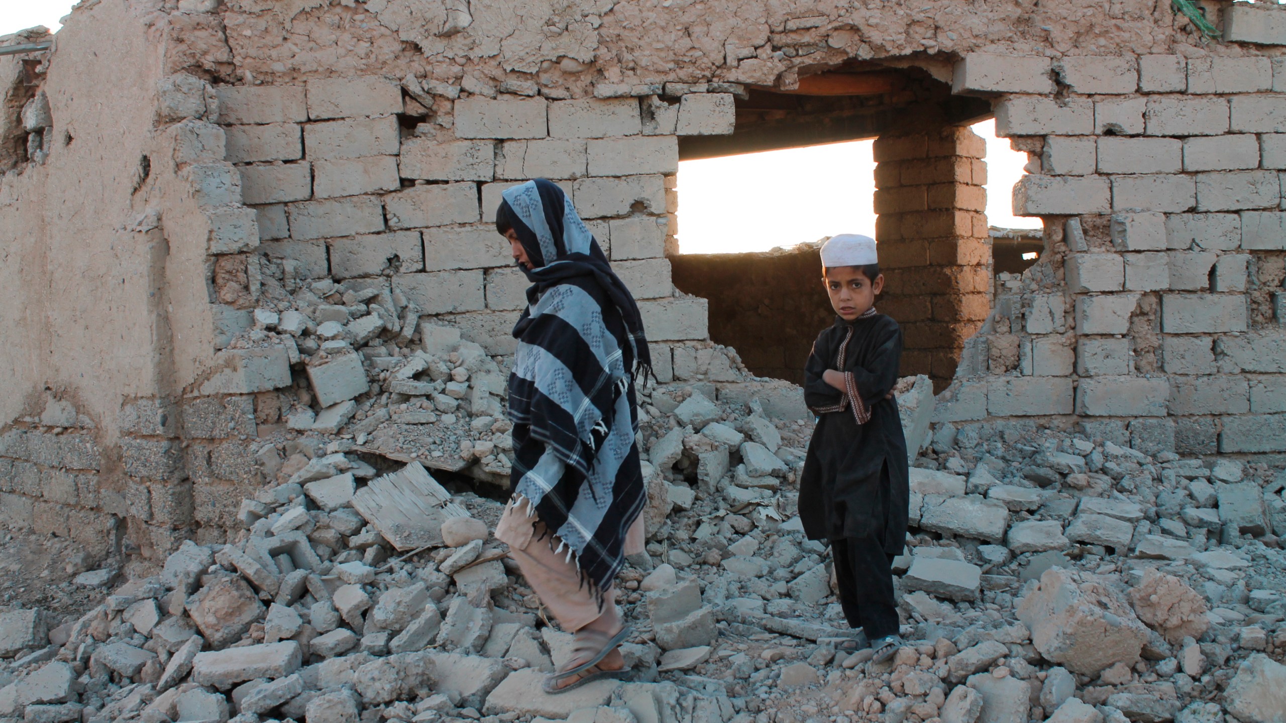 Afghan boys walk near a damaged house after airstrikes in two weeks ago during a fight between government forces and the Taliban in Lashkar Gah, Helmand province, southwestern, Afghanistan, Saturday, Aug. 21, 2021. (AP Photo/Abdul Khaliq)