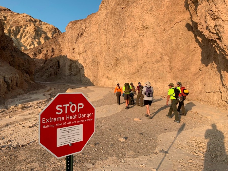 In this Wednesday, Aug. 18, 2021, photo provided by the National Park Service, an inter-agency search and rescue crew walks past a sign reading" "Stop, Extreme Heat Danger," with park rangers responding on foot near Red Cathedral along the Golden Canyon Trail in Death Valley National Park, Calif. (National Park Service via AP)