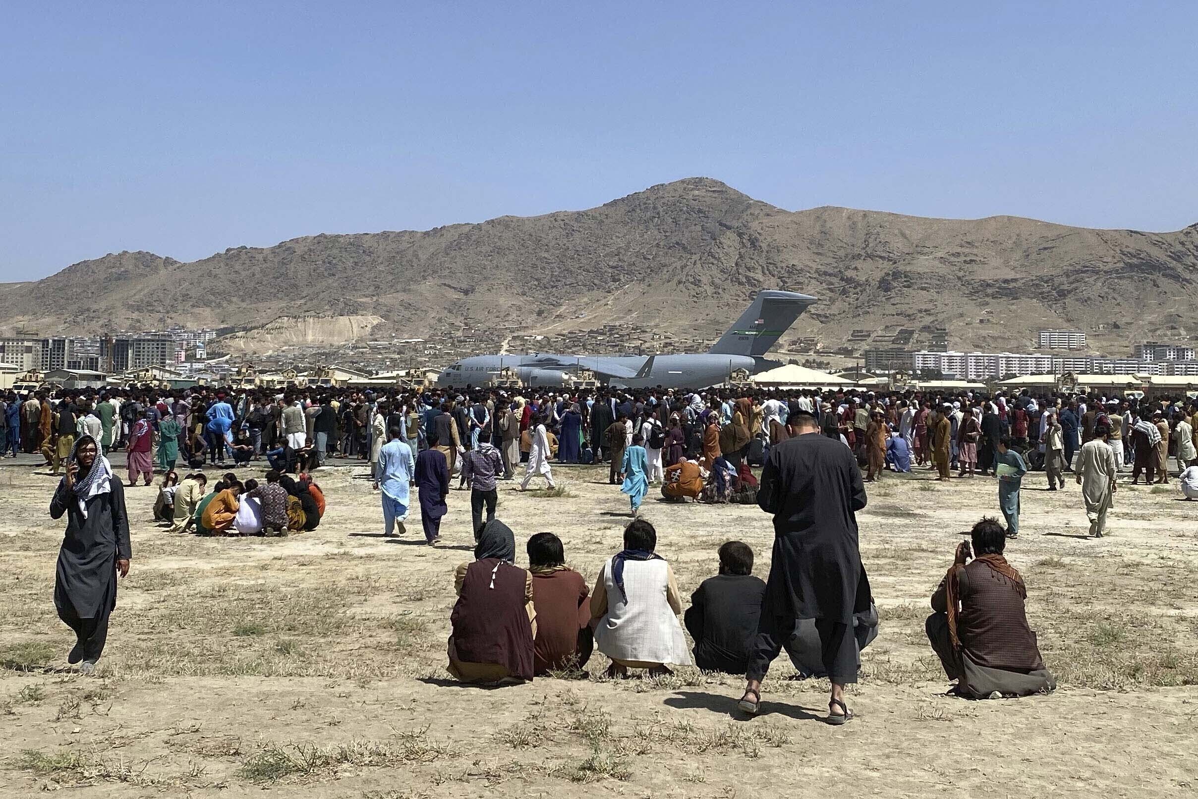 In this Aug. 16, 2021, file photo hundreds of people gather near a U.S. Air Force C-17 transport plane along the perimeter at the international airport in Kabul, Afghanistan. After the Taliban takeover, employees of the collapsed government, civil society activists and women are among the at-risk Afghans who have gone into hiding or are staying off the streets. They hope for a way to leave their homeland. (AP Photo/Shekib Rahmani, File)