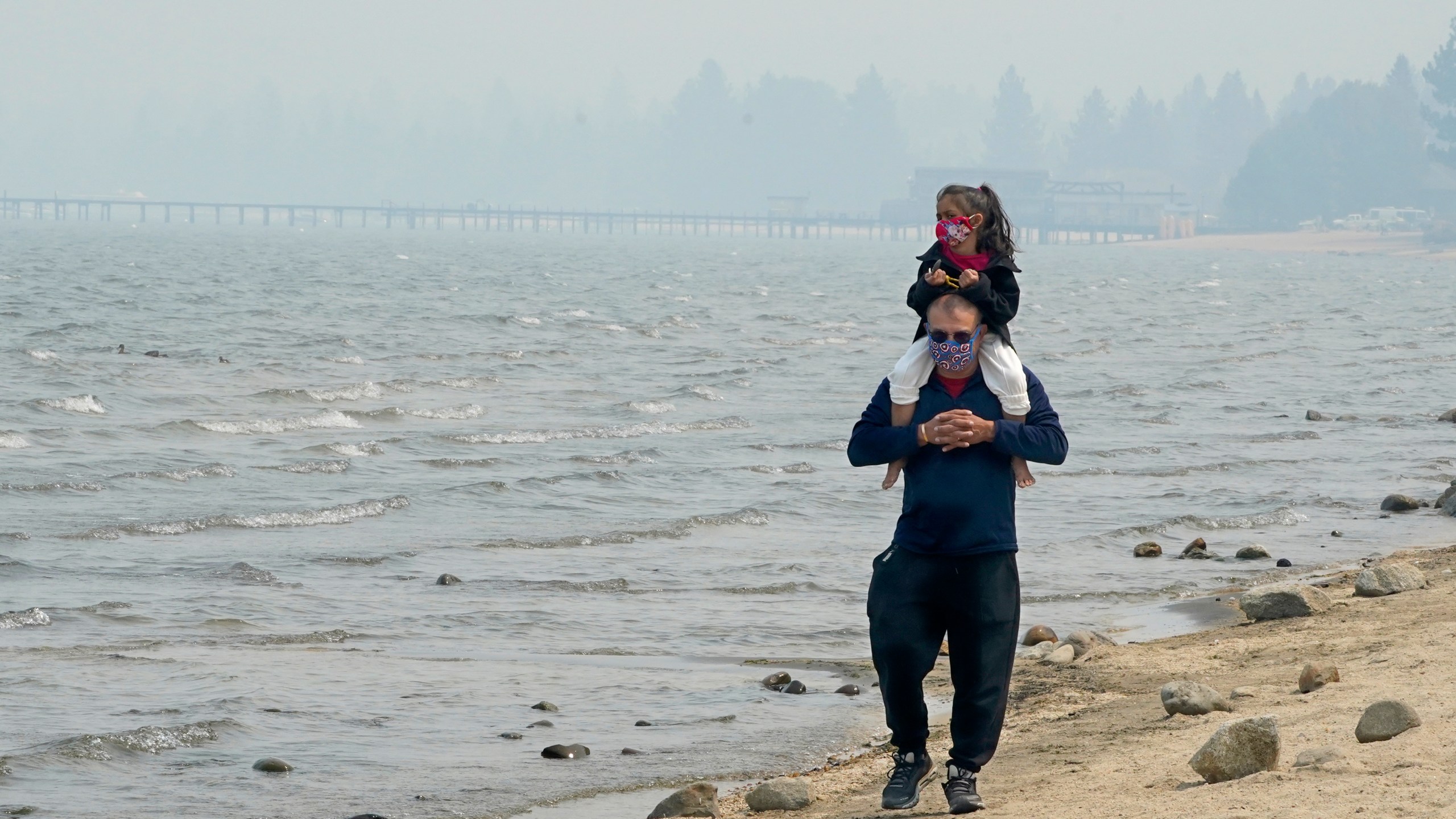 Presley Mila Perez gets a ride on the shoulders of George Estrada as they walk along the shore of Lake Tahoe in South Lake Tahoe on Aug. 24, 2021. (Rich Pedroncelli / Associated Press)