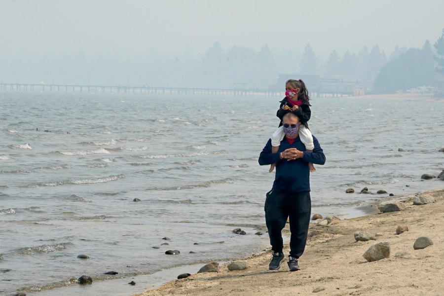 Presley Mila Perez gets a ride on the shoulders of George Estrada as they walk along the shore of Lake Tahoe in South Lake Tahoe on Aug. 24, 2021. (Rich Pedroncelli / Associated Press)