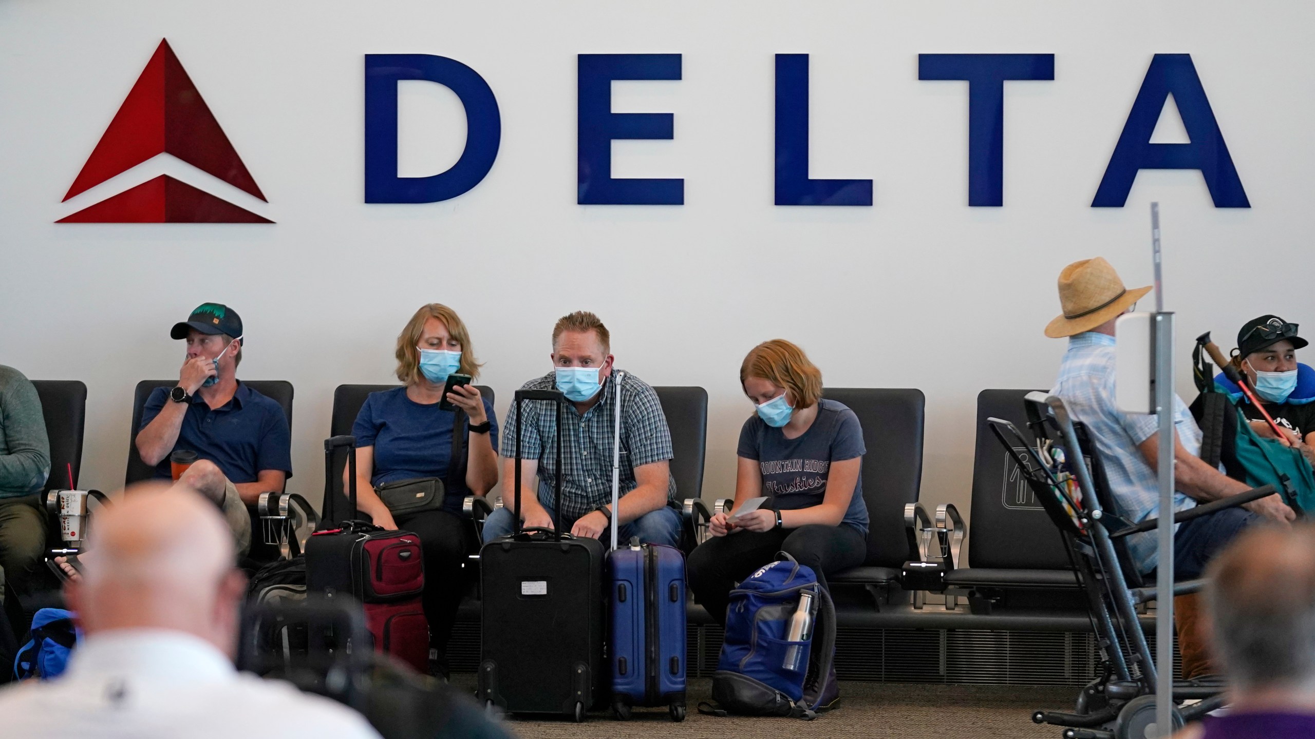 People sit under Delta sign at Salt Lake City International Airport on July 1, 2021, in Salt Lake City. Delta Air Lines won't force employees to get vaccinated, but it's going to make unvaccinated workers pay a $200 monthly charge. Delta said Wednesday, Aug. 25, 2021 that it will also require weekly testing for unvaccinated employees starting next month, although the airline says it'll pick up the cost of that testing. (AP Photo/Rick Bowmer, file)