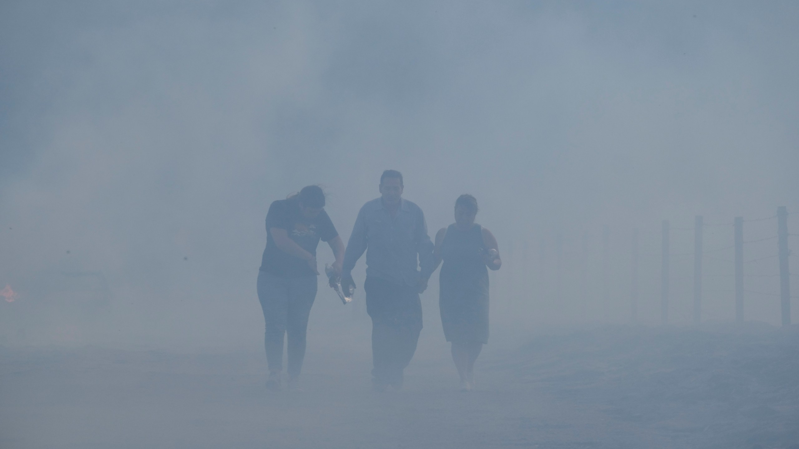 Homeowners Jose Lamas, center, his wife, Maria Covarrubias, right, and his daughter Astrid Covarrubias walk through the smoke after visiting their burned-out home from the South Fire in Lytle Creek, San Bernardino County, on Aug. 25, 2021. (Ringo H.W. Chiu / Associated Press)