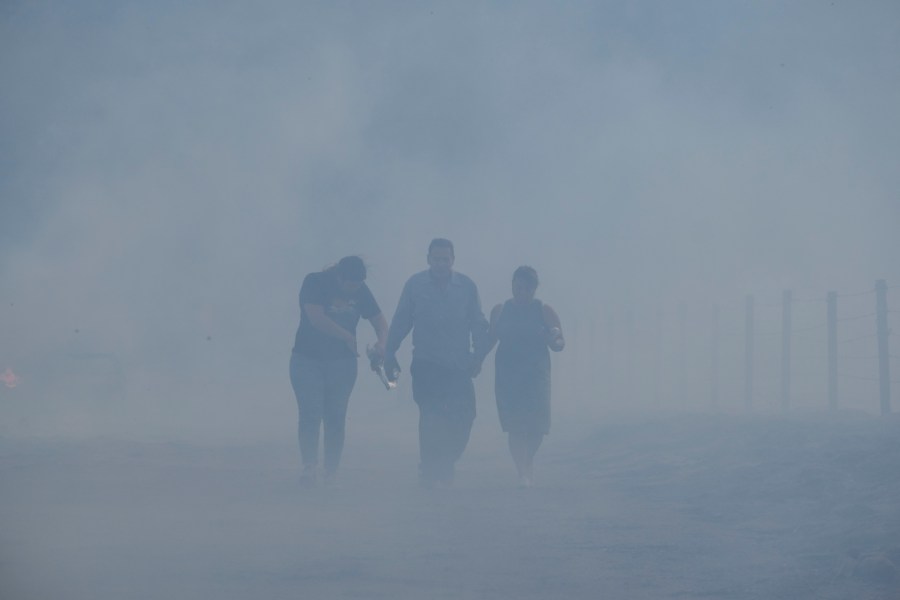 Homeowners Jose Lamas, center, his wife, Maria Covarrubias, right, and his daughter Astrid Covarrubias walk through the smoke after visiting their burned-out home from the South Fire in Lytle Creek, San Bernardino County, on Aug. 25, 2021. (Ringo H.W. Chiu / Associated Press)